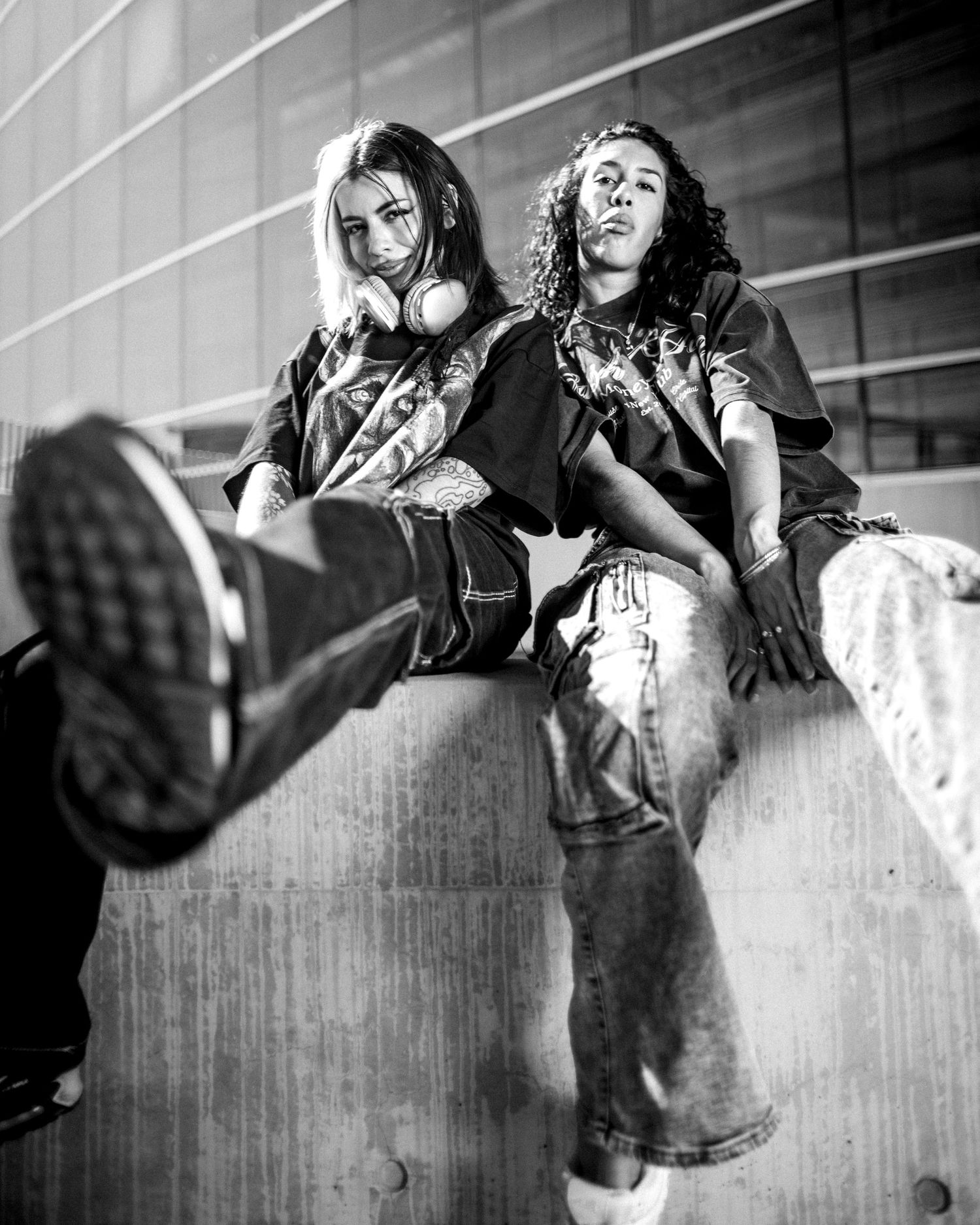 Two young women pose confidently in black and white urban street style fashion photo.