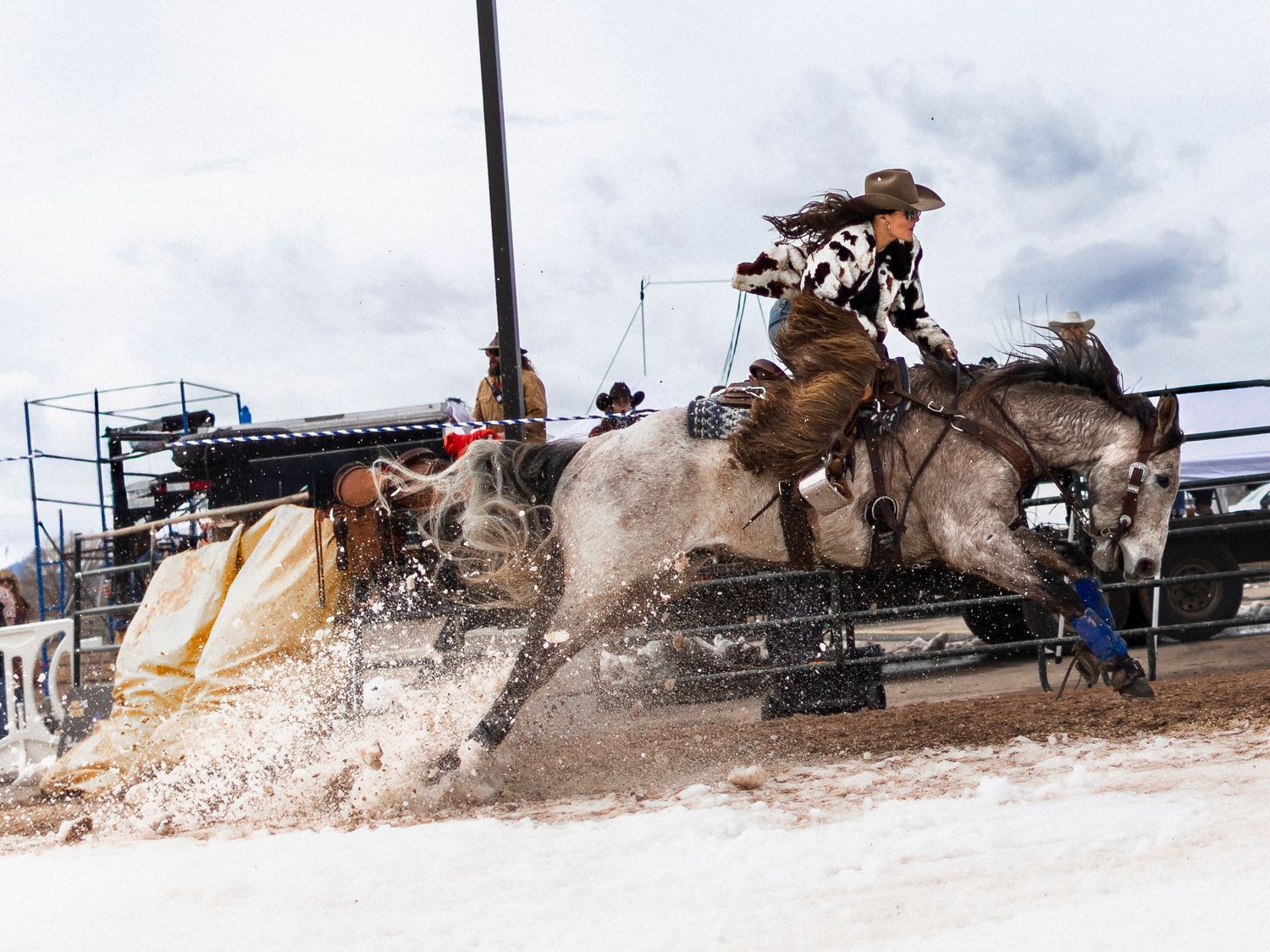 Cowboy riding gray horse splashing through water at a rodeo event with dramatic action and crowd in background.