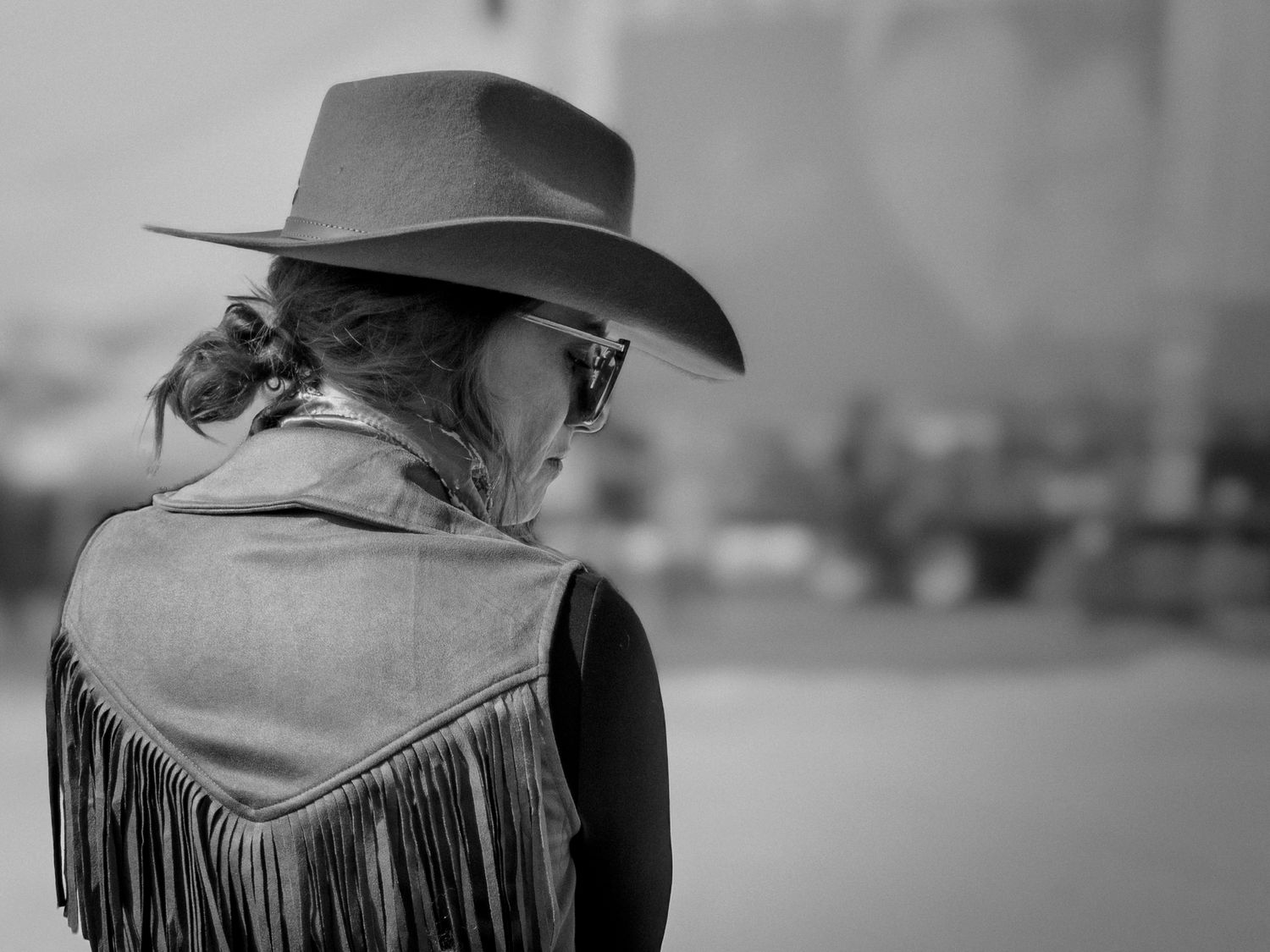 Black and white rear view of woman wearing cowboy hat and fringed suede vest.