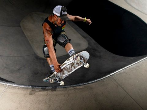 Skateboarder grinding the edge of a concrete bowl ramp at an outdoor skate park.