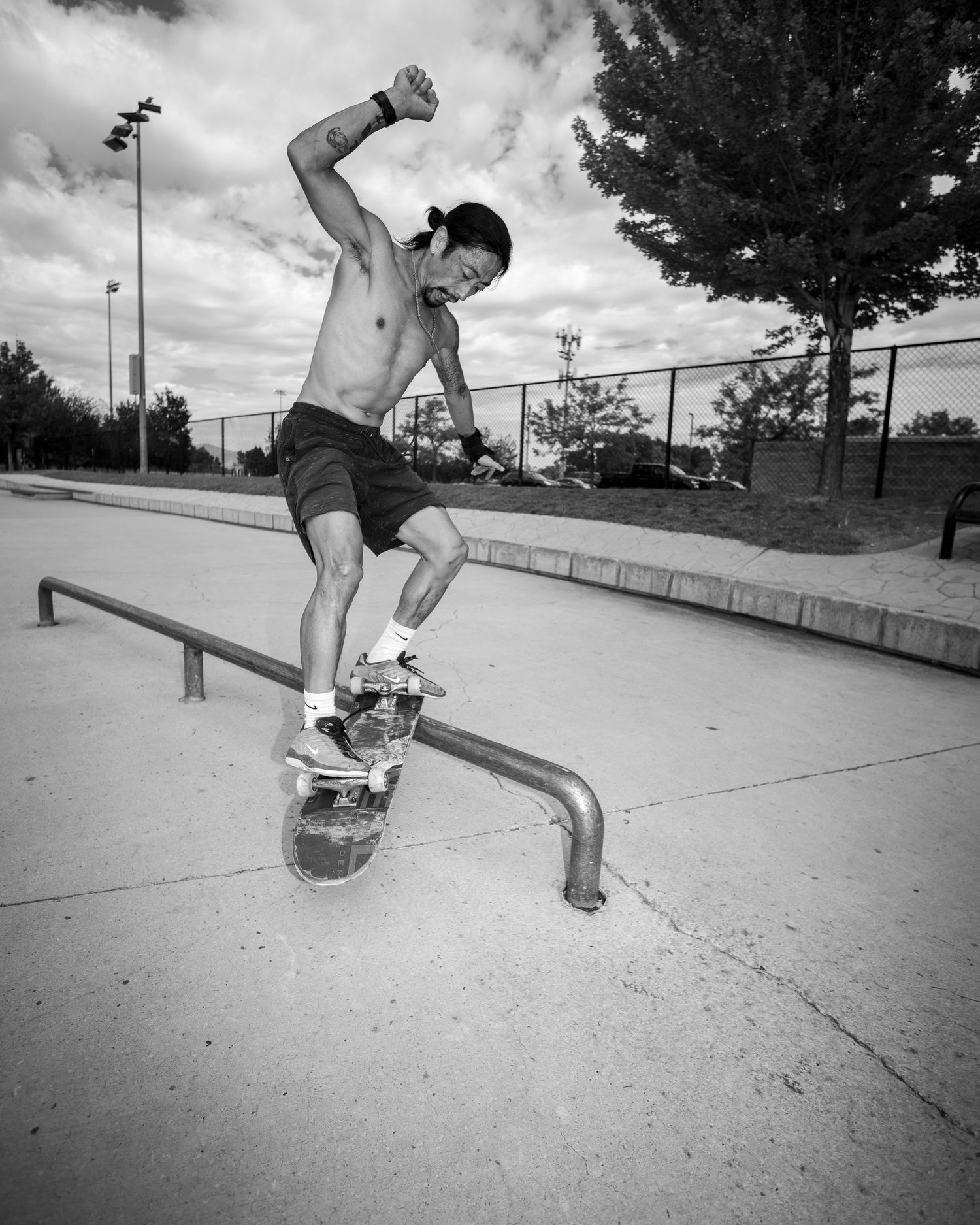 Shirtless skateboarder performing a grind trick on a metal rail at an outdoor skate park in black and white.