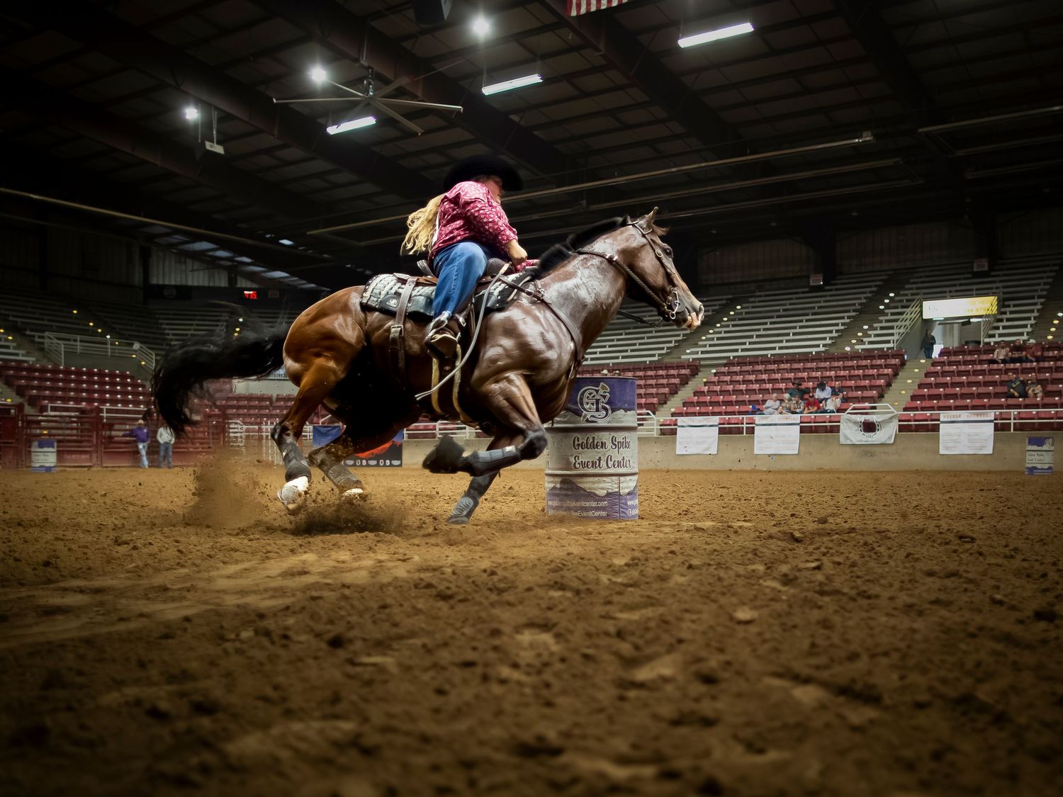 Barrel racing competitor on horseback rounding a barrel in an indoor rodeo arena.