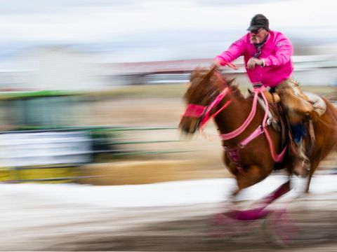A rider in bright pink jacket races on horseback in a thrilling motion-blurred competition.