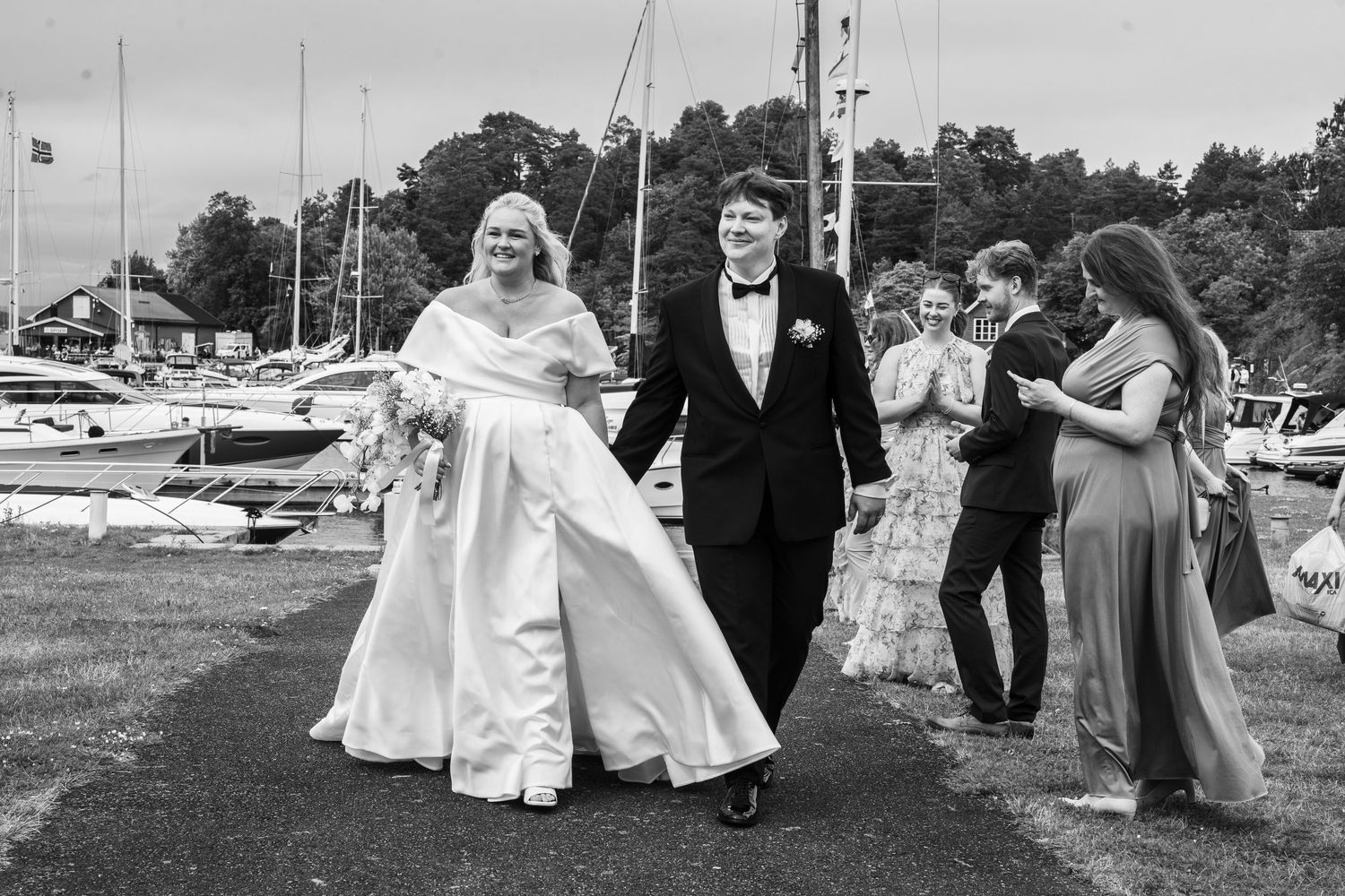 Bride and groom walking with wedding guests at a marina in black and white photo.