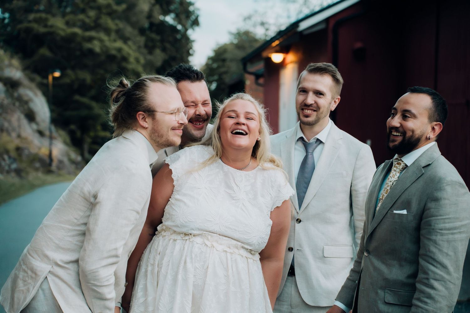 Bride and four groomsmen laughing joyfully together outdoors at a wedding celebration.