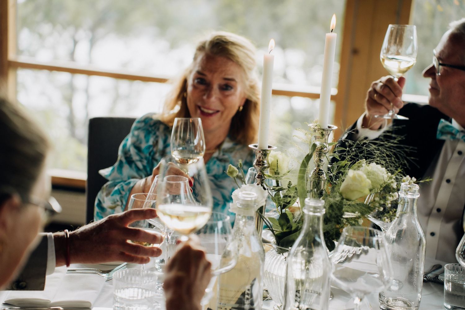 Wedding guests raising glasses of white wine in a toast at an elegant reception table.