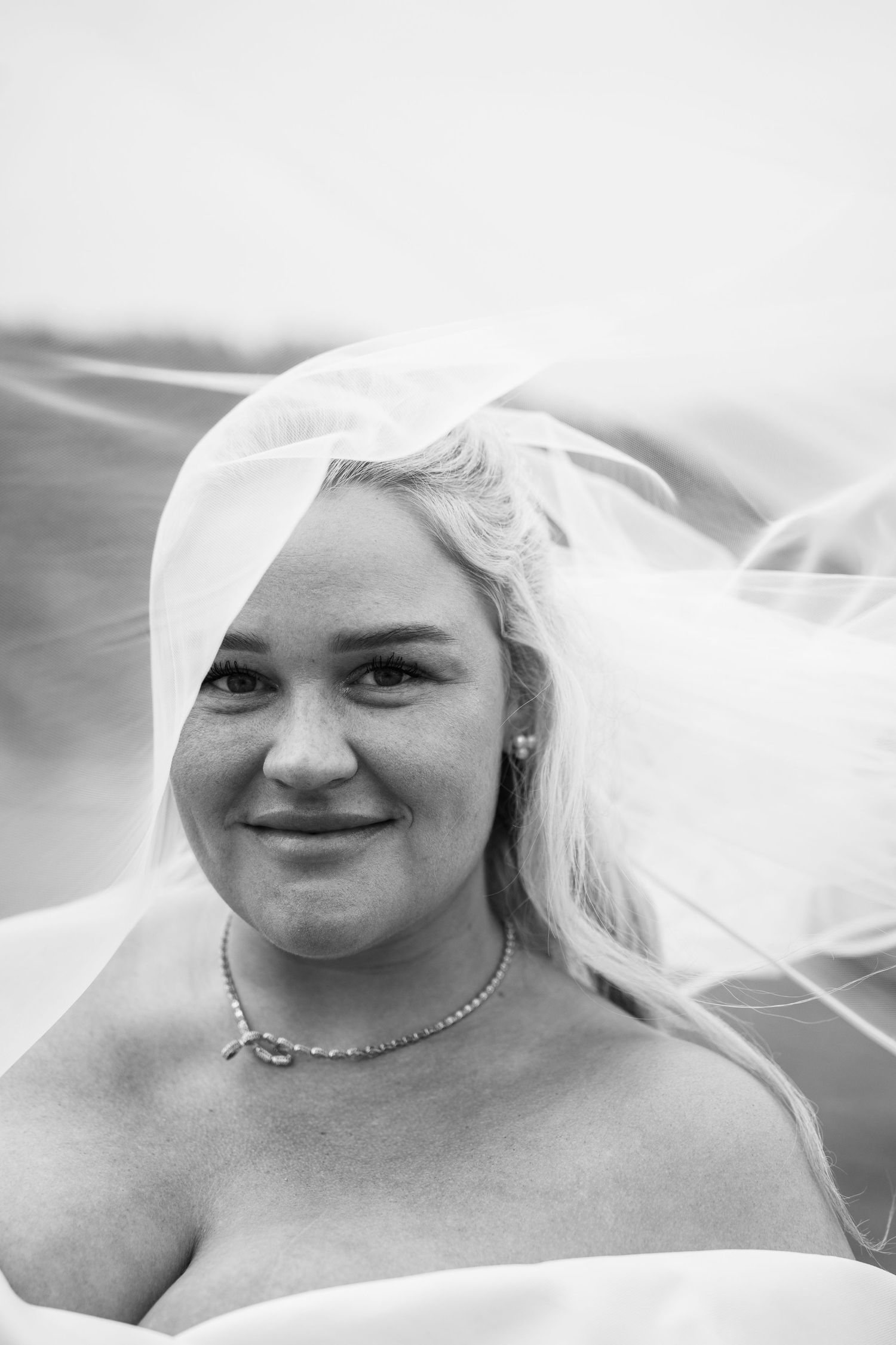 Bride smiling with veil blowing in wind, black and white wedding portrait.