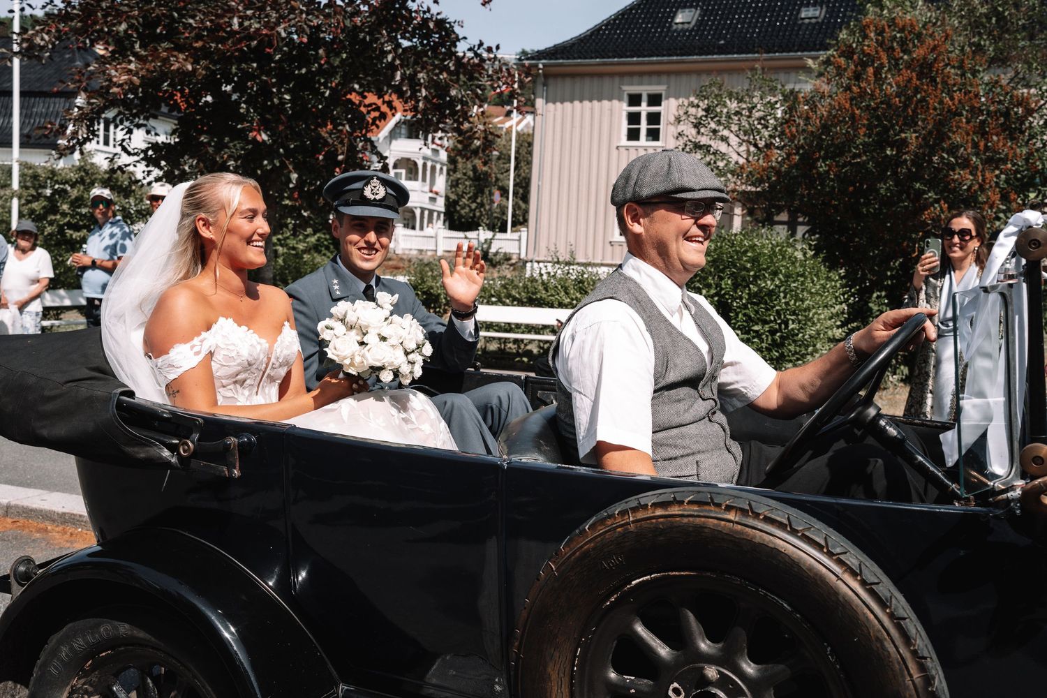 Brud og brudgom kjører i en vintage svart kabriolet på bryllupsdagen.