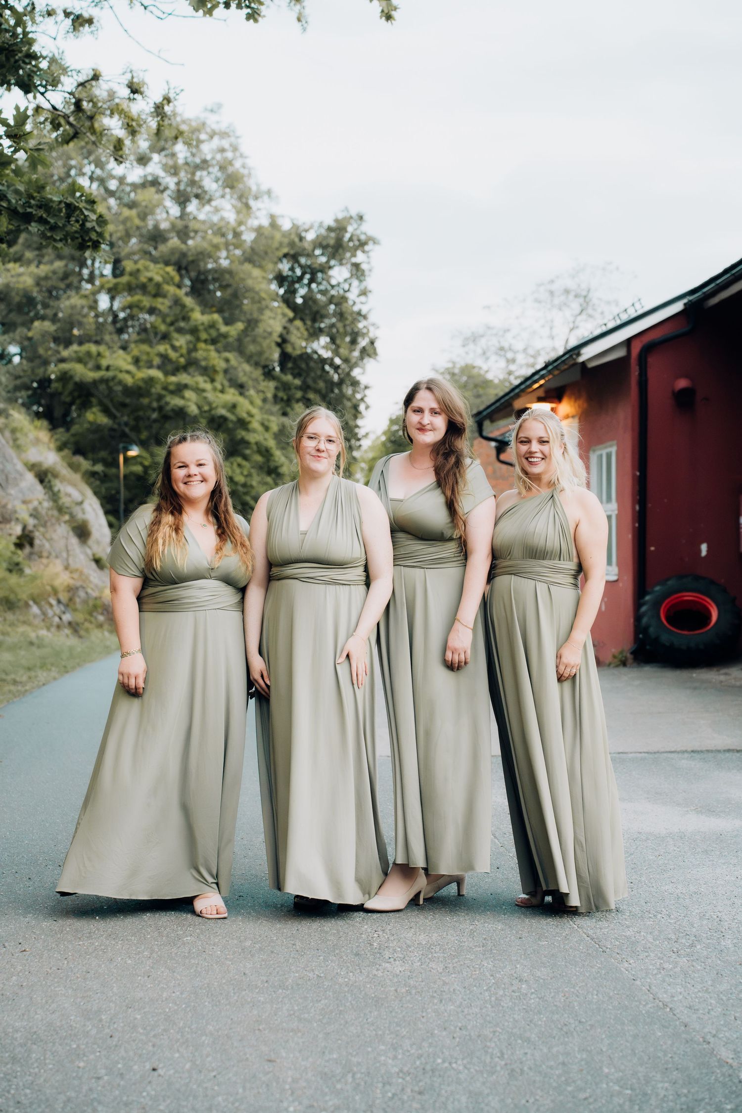 Four bridesmaids posing in matching sage green multiway dresses at an outdoor wedding venue.