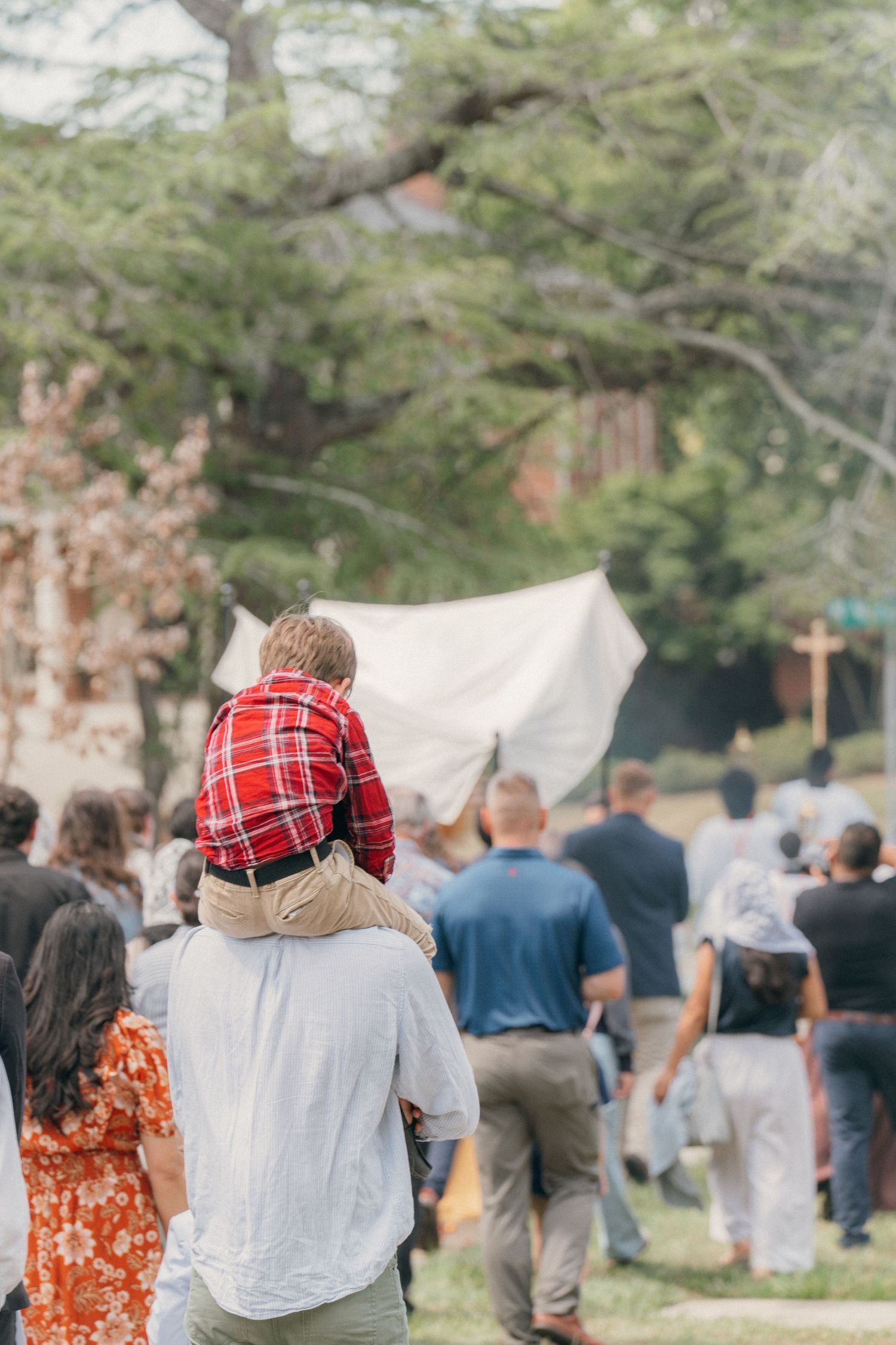 Father carrying his son on his shoulders while following a Corpus Christi procession