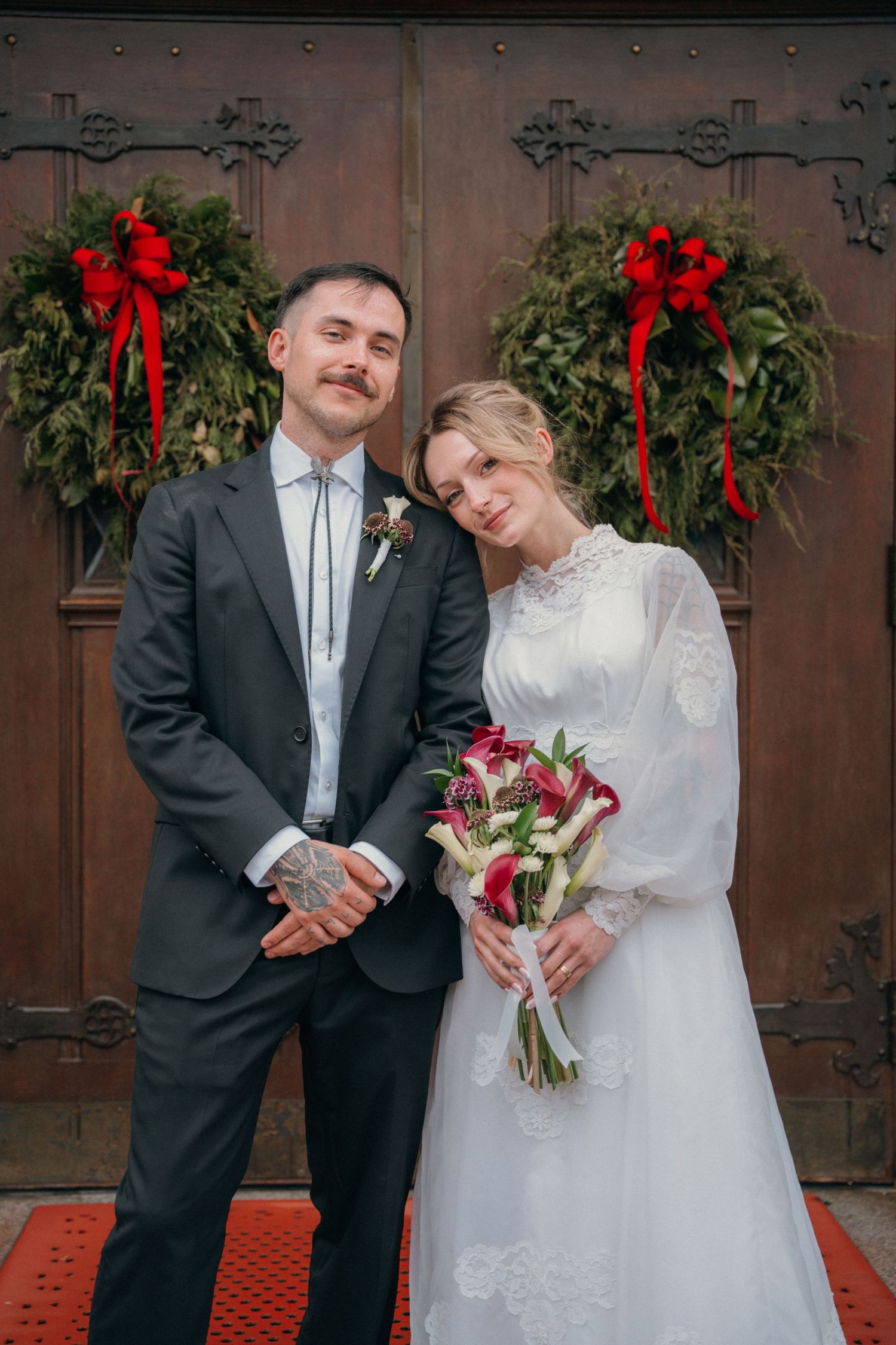Bride and groom at church doors decorated with Christmas wreaths and red bows