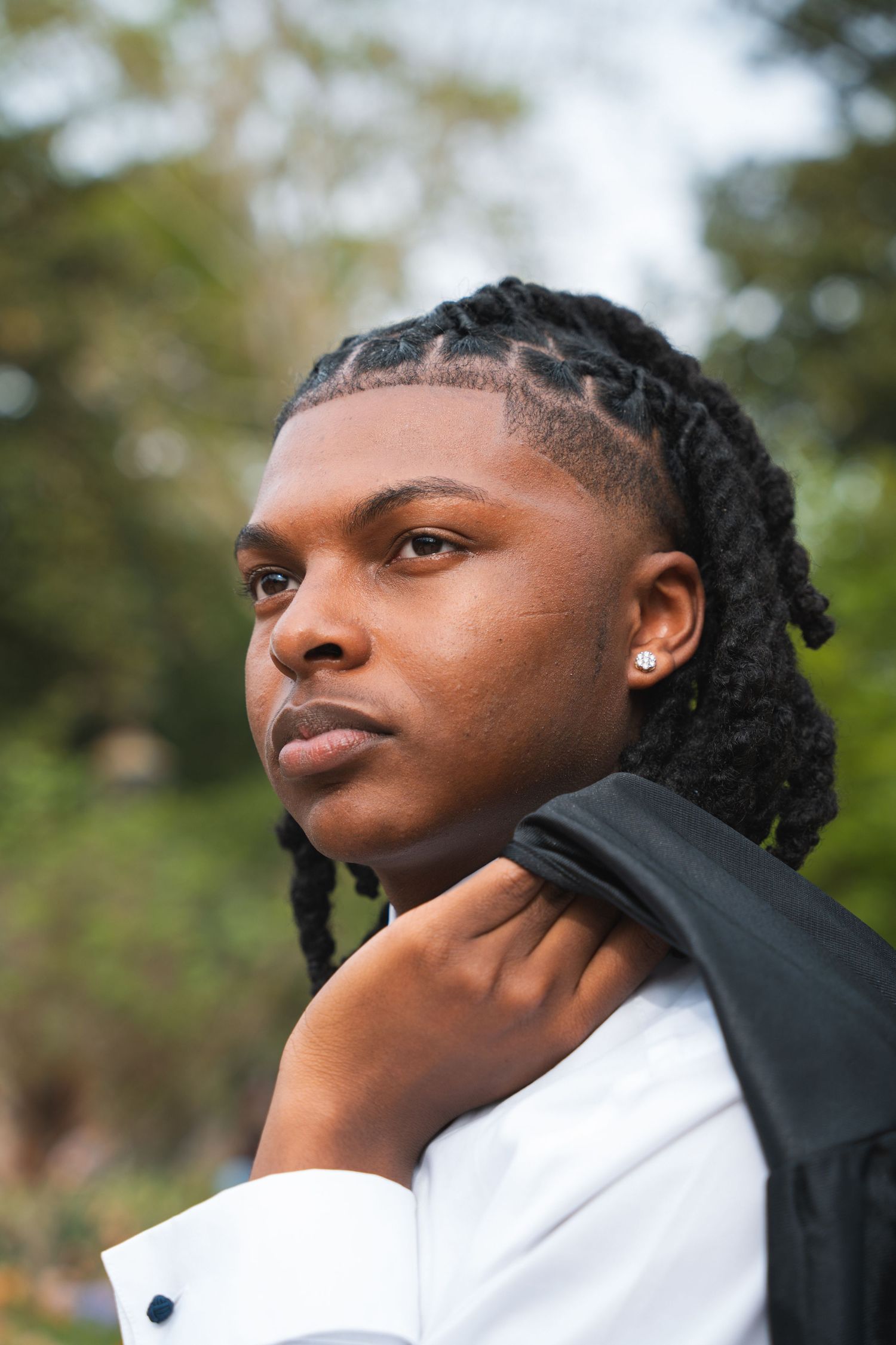 Graduate with his gown over his shoulder looking off into a green garden