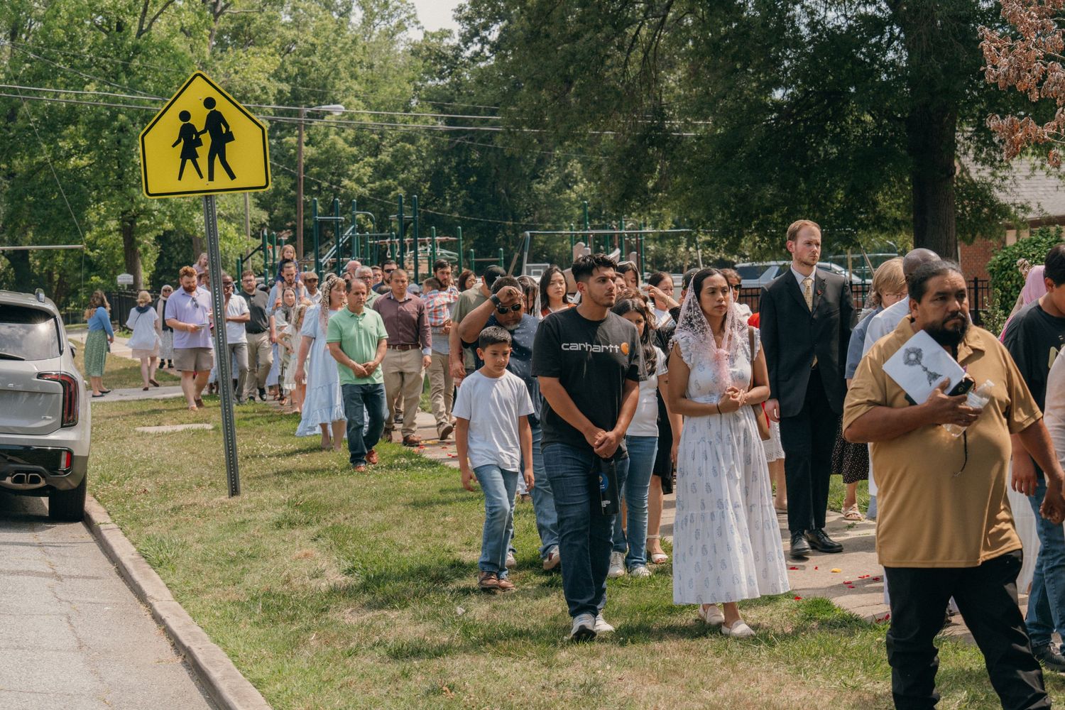 Catholic parishioners walking along a tree-lined street in a Corpus Christi procession