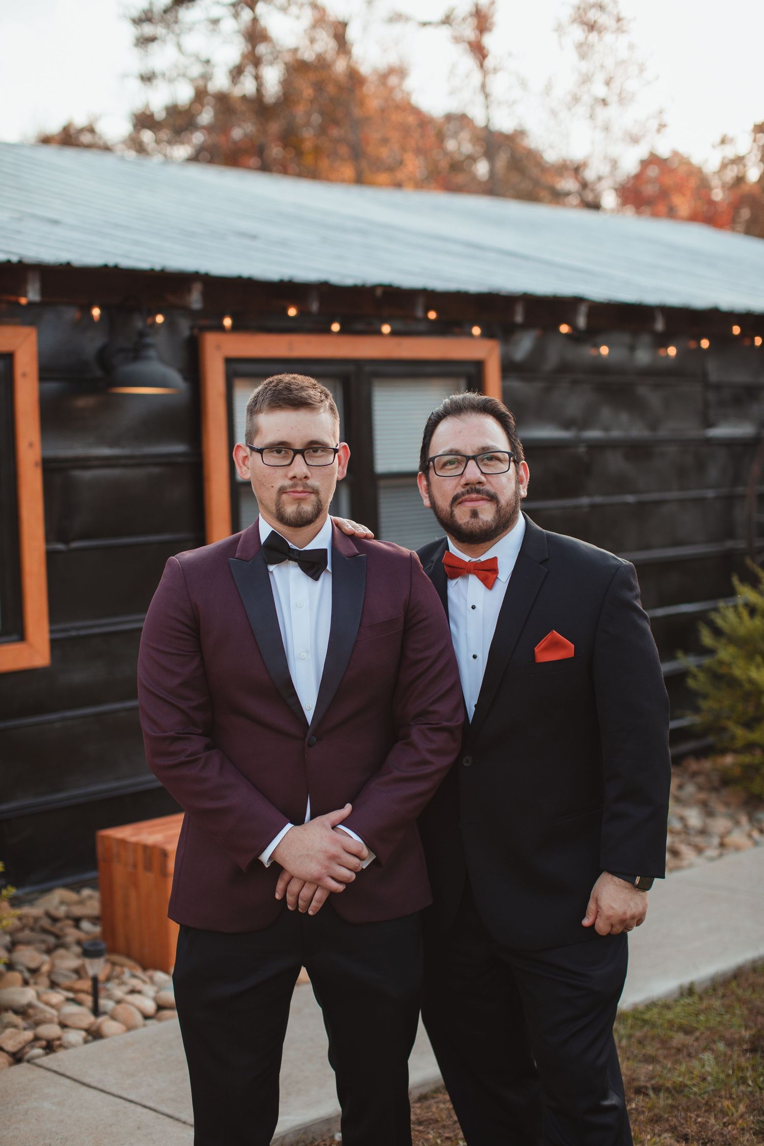 Groom in a burgundy tuxedo jacket with his best man outside a rustic barn venue