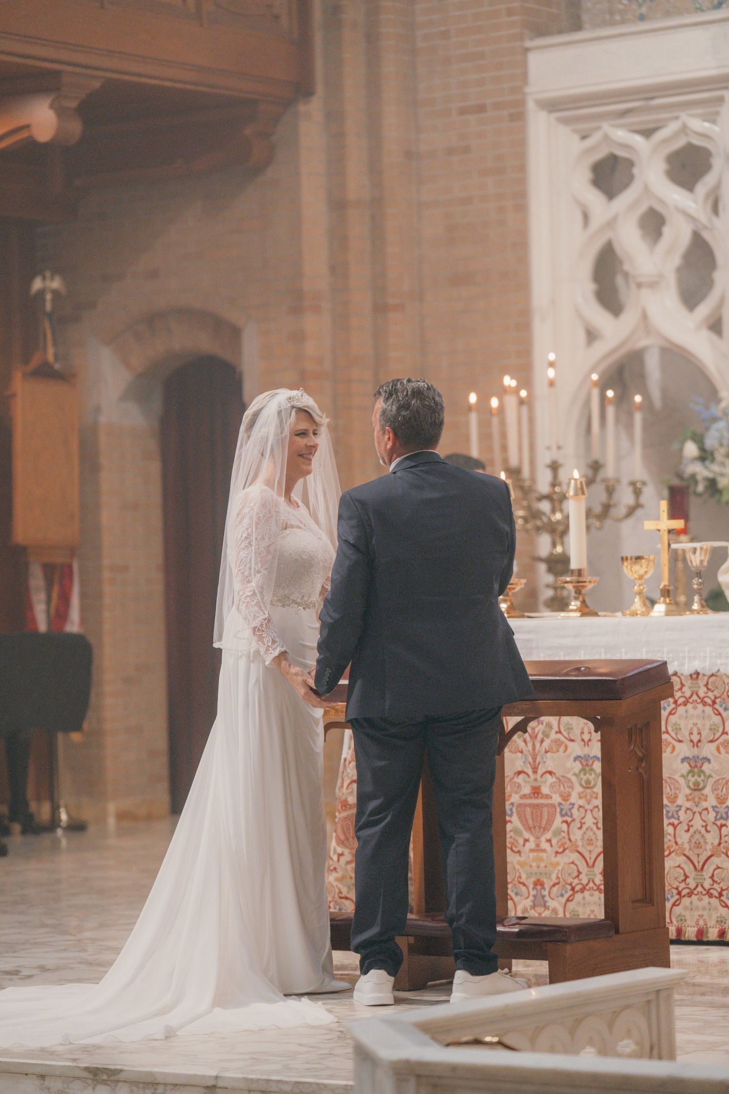 Bride in a long veil standing with the groom before the altar