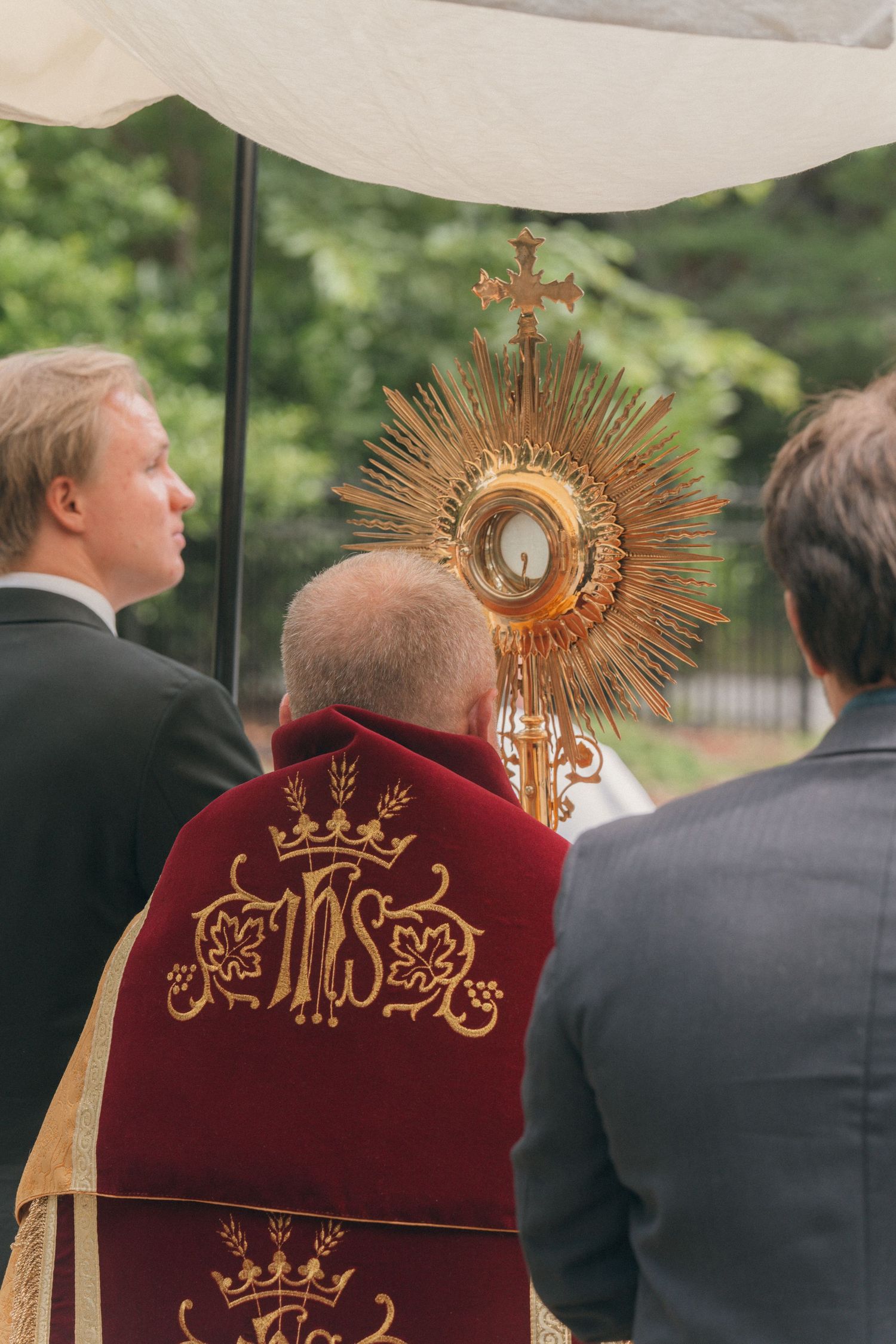 Priest in a red and gold humeral veil holding the monstrance aloft during a Eucharistic procession