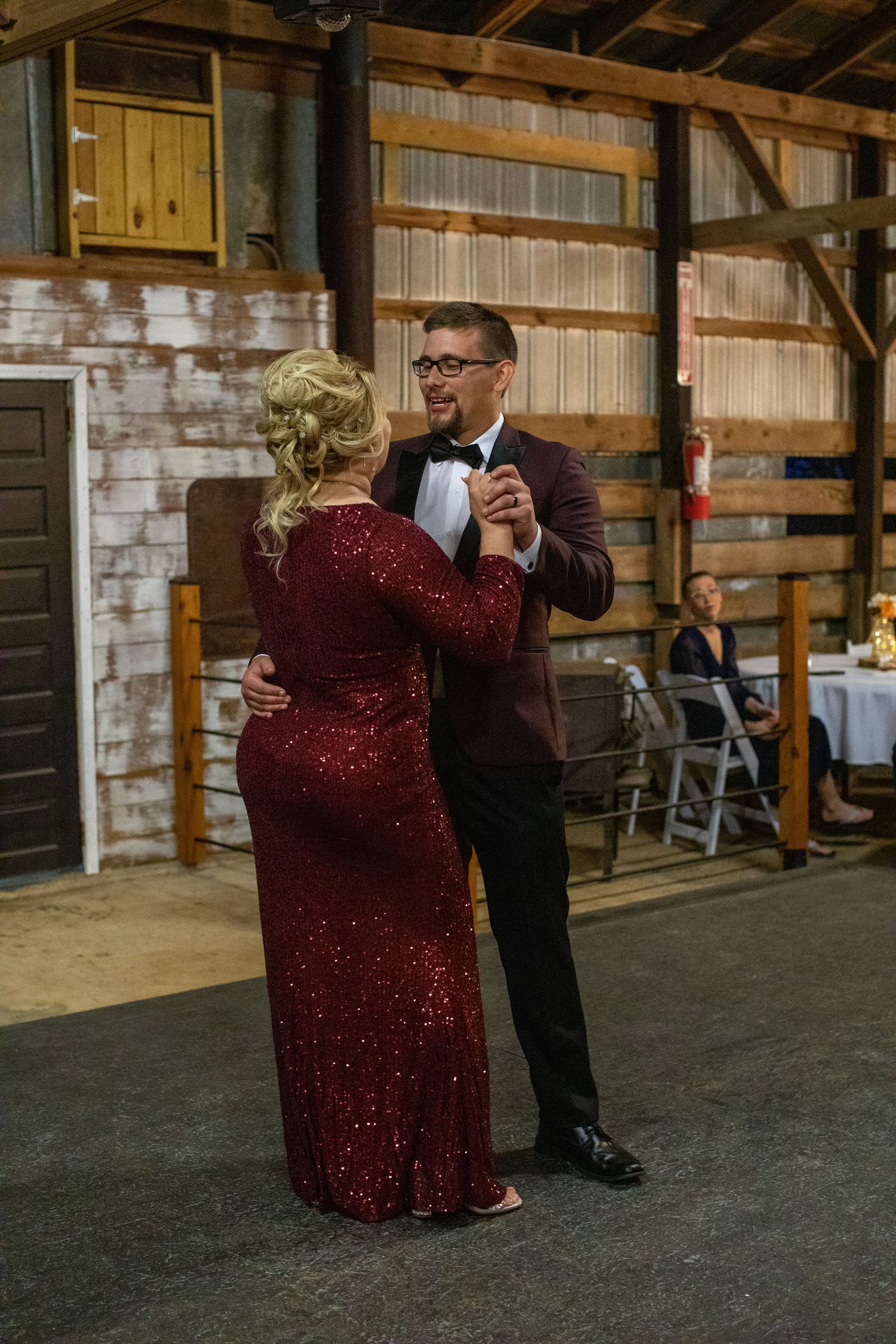 Groom sharing a dance with a woman in a burgundy gown in the barn