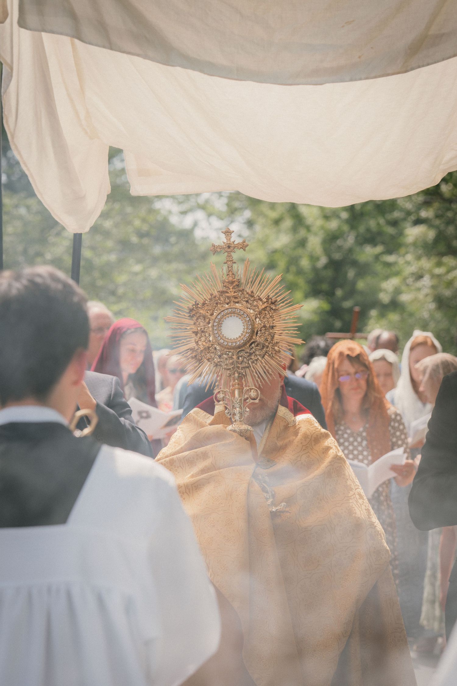 Monstrance glowing through incense smoke beneath a white canopy at a Corpus Christi procession
