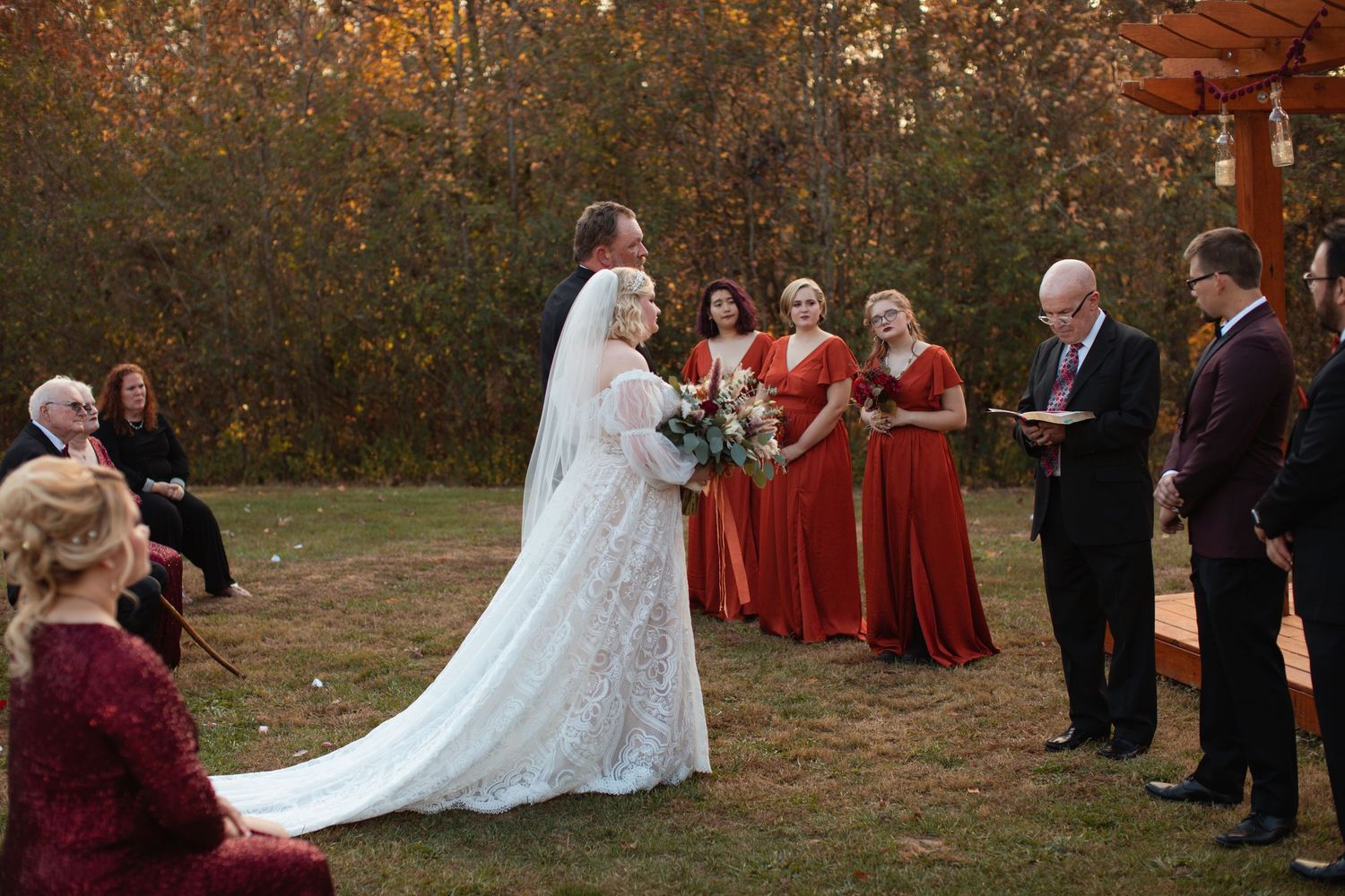 Bride and groom saying vows with the wedding party in burgundy beside them