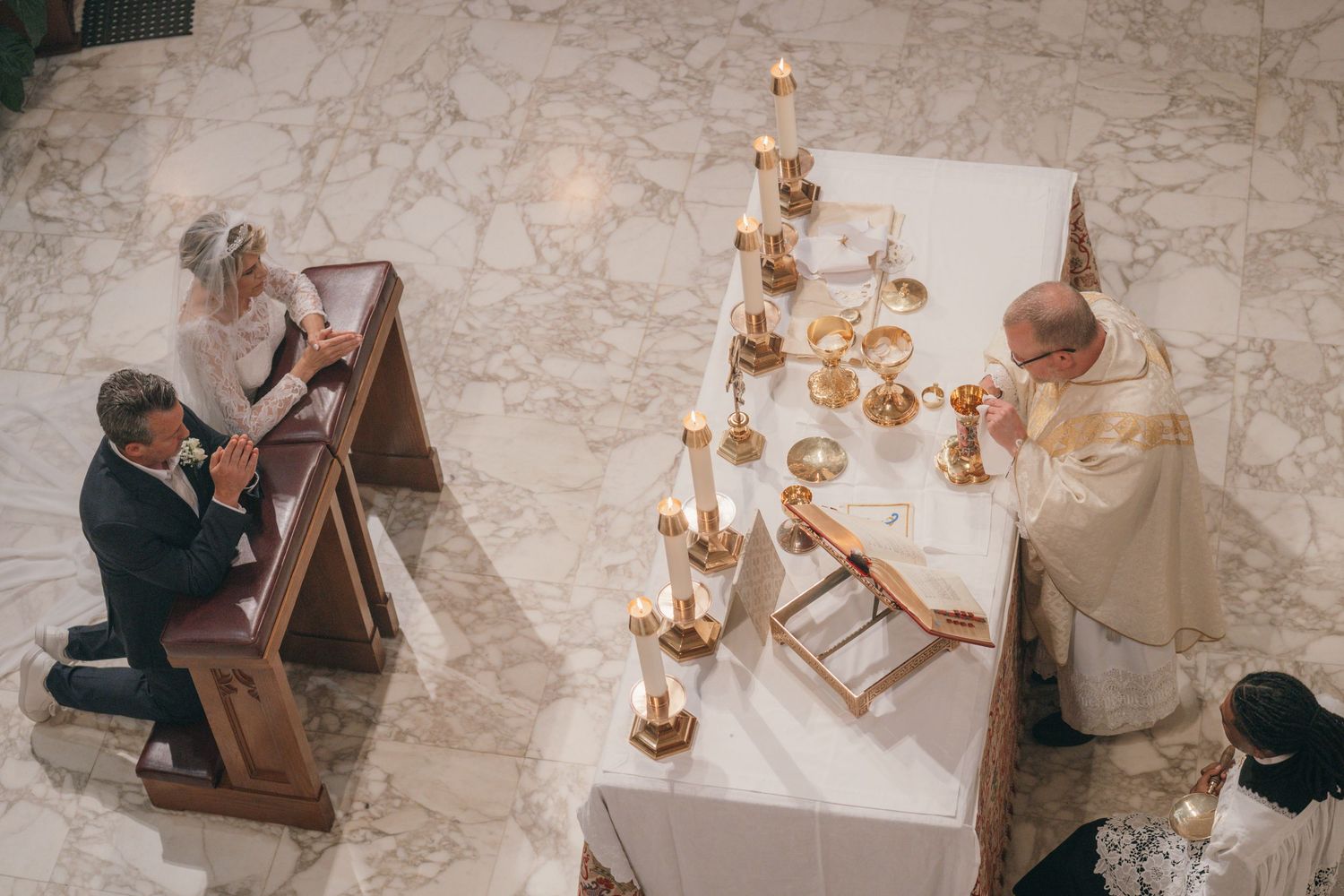 Bride and groom kneeling near the altar as the priest celebrates Mass