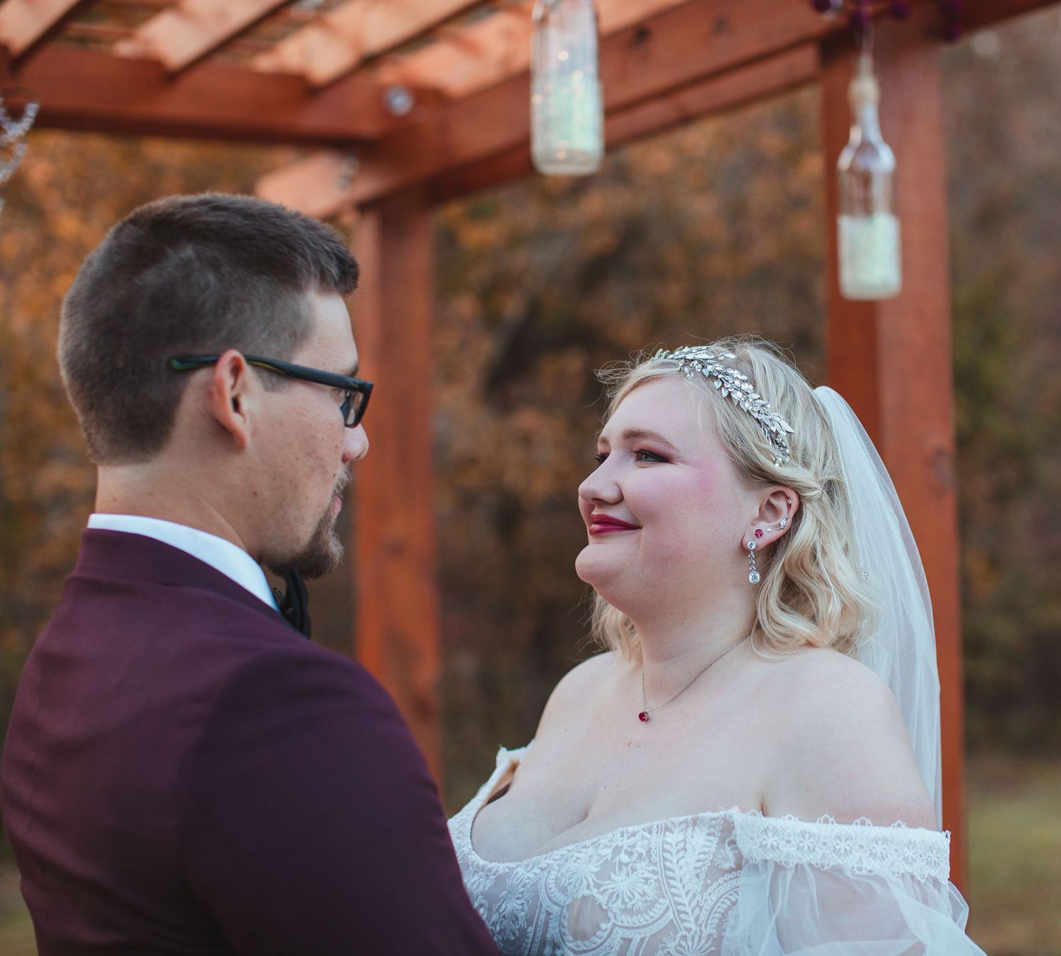 Bride and groom smiling at each other under a wooden pergola