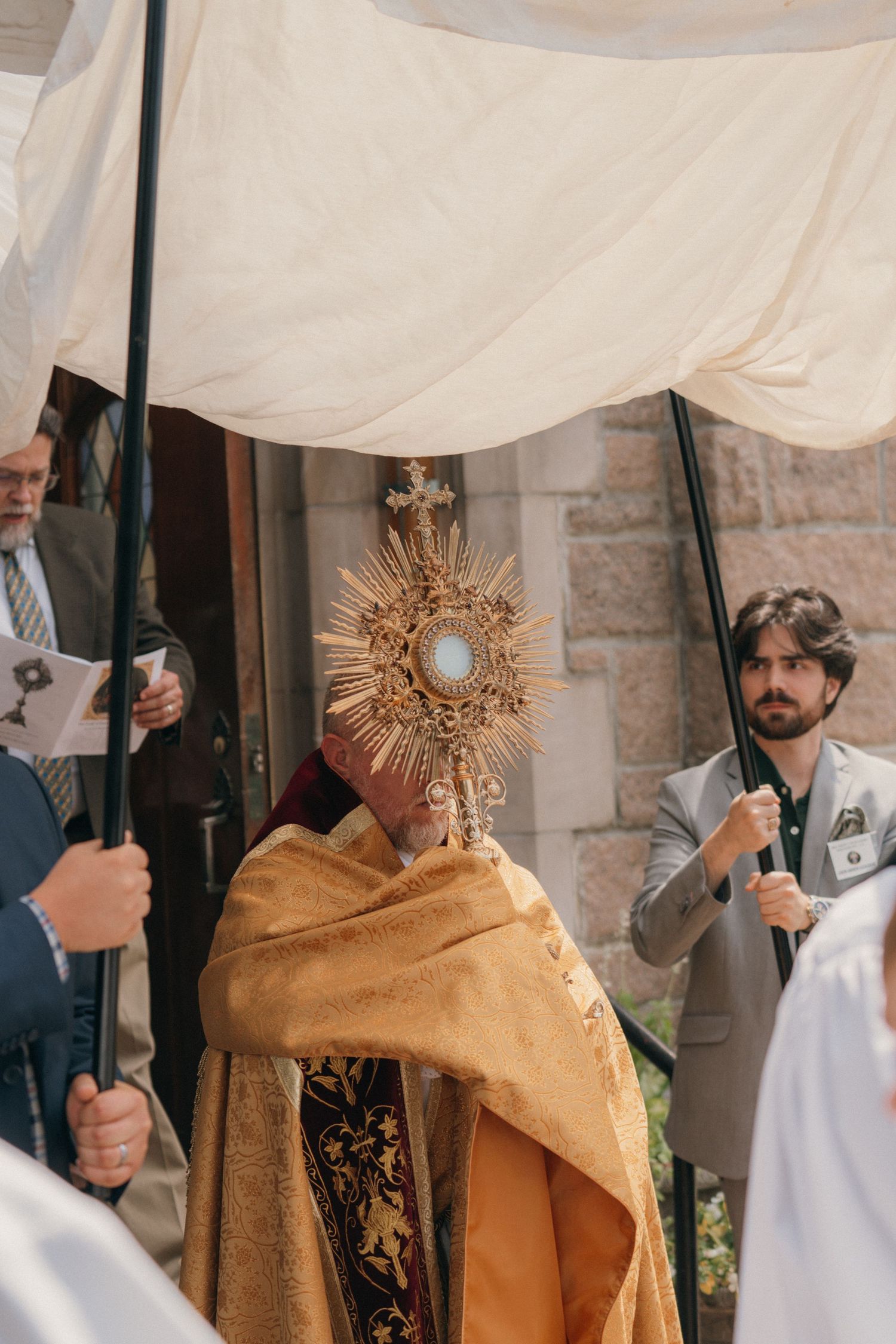 Priest in gold vestments holding the monstrance beneath the canopy at the church doors