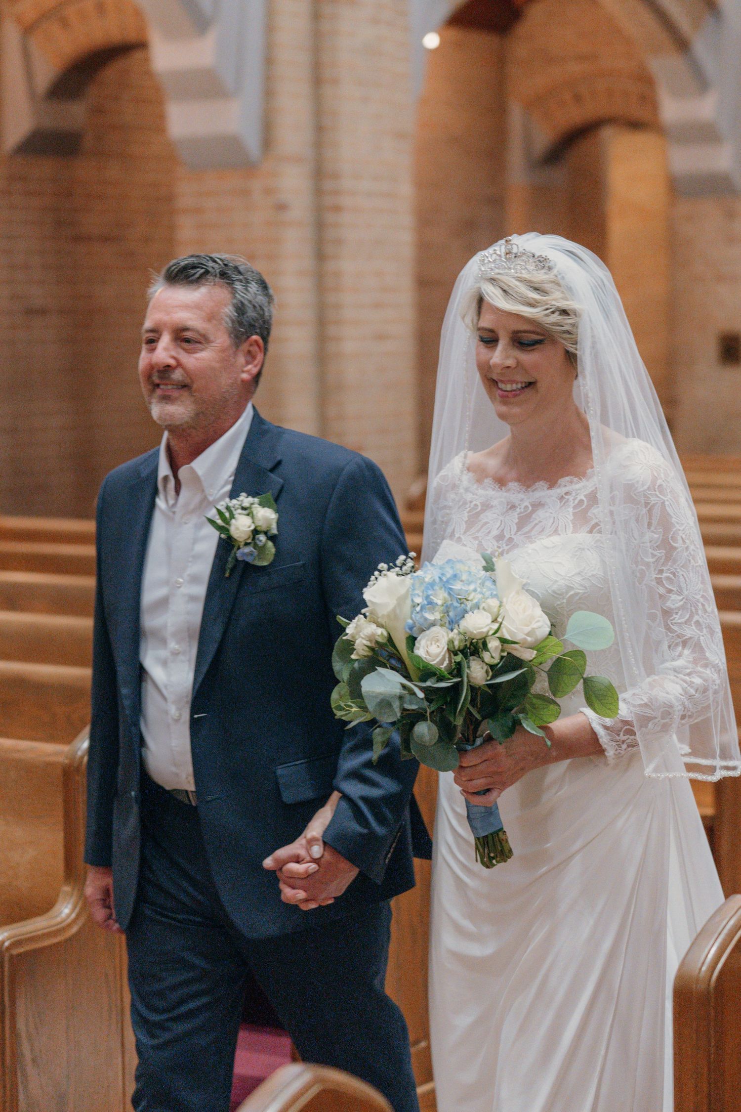 Bride and her father walking down the aisle with a blue and white bouquet