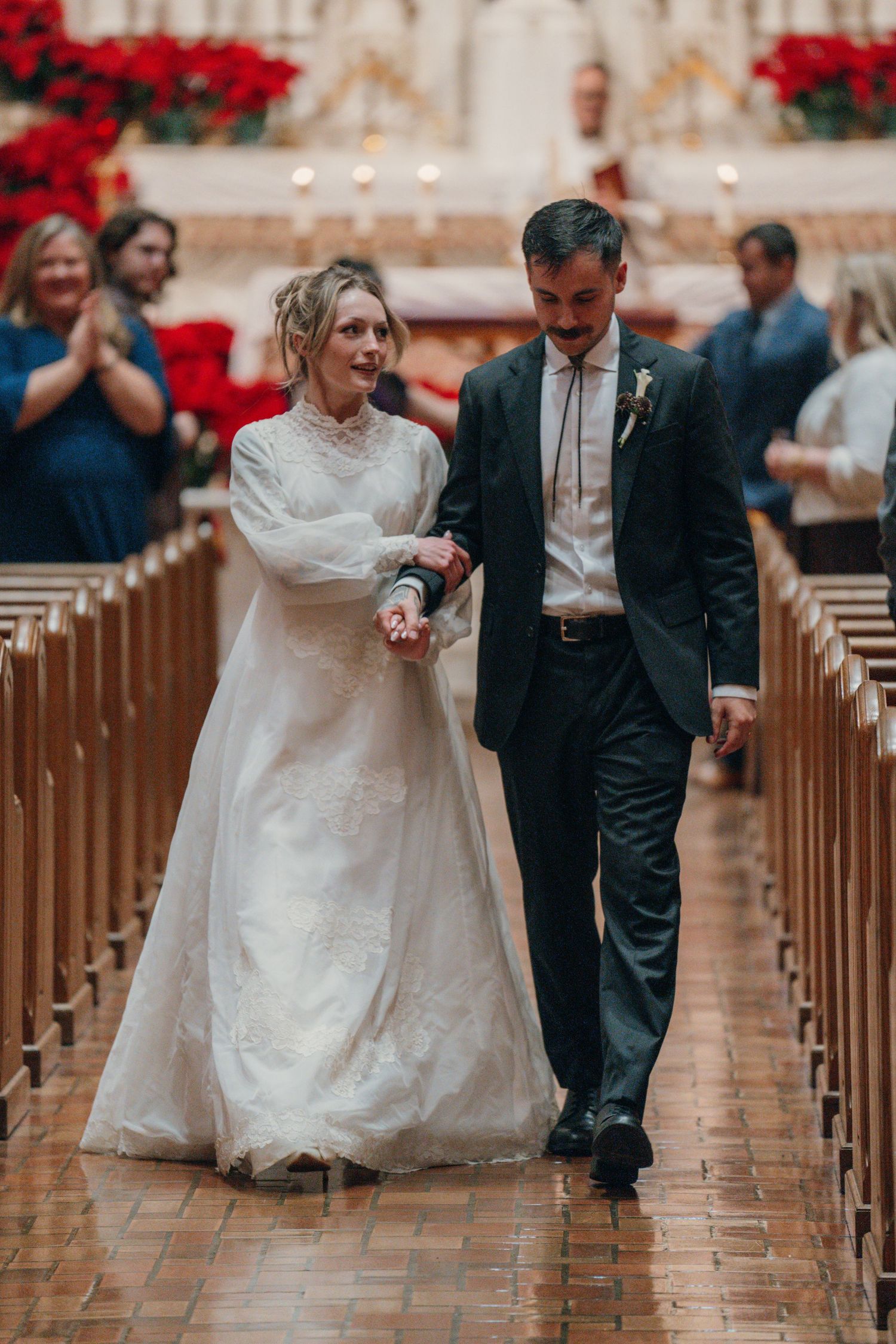 Bride and groom walking down the aisle past poinsettias after their wedding
