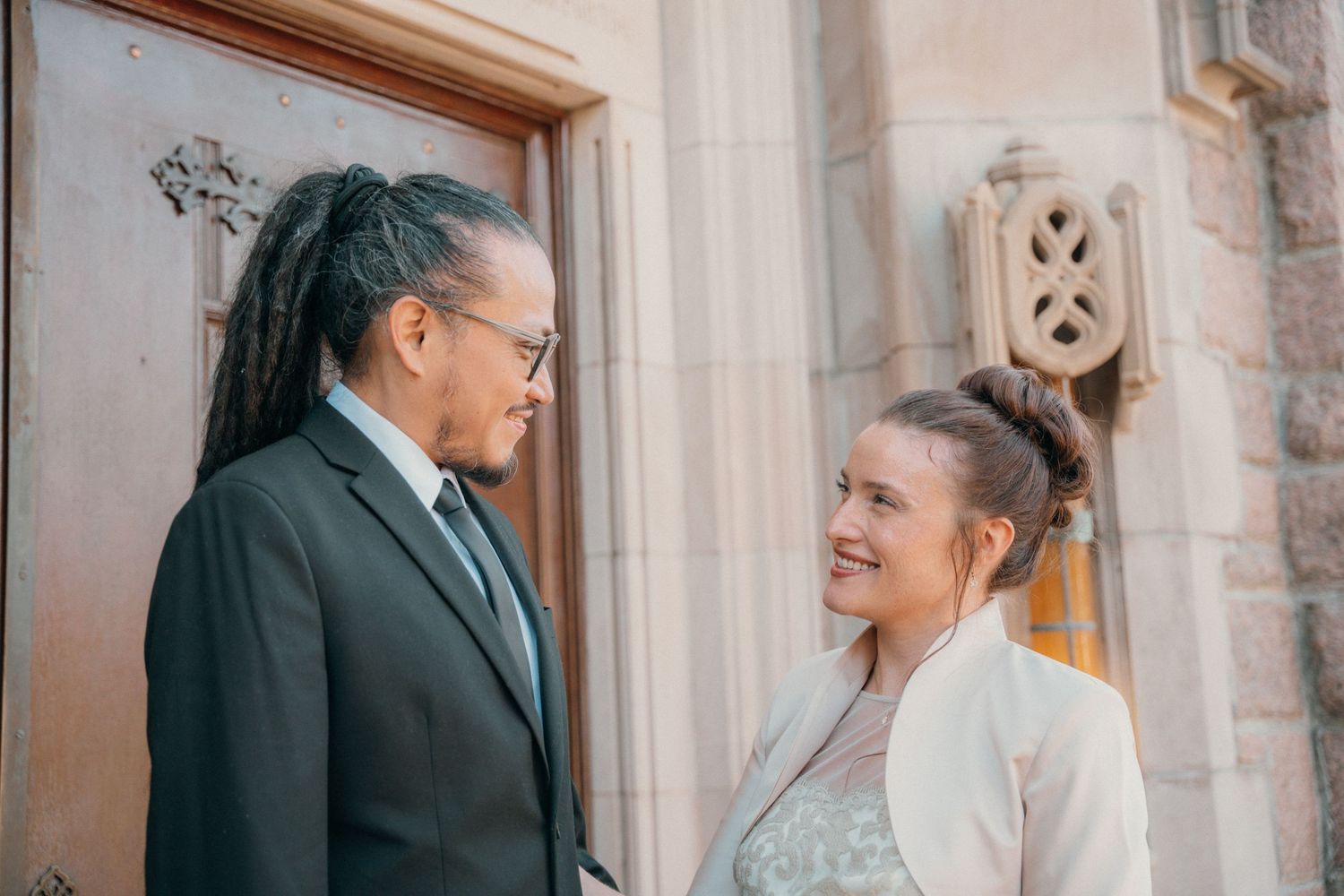Groom and bride smiling at each other in a church doorway