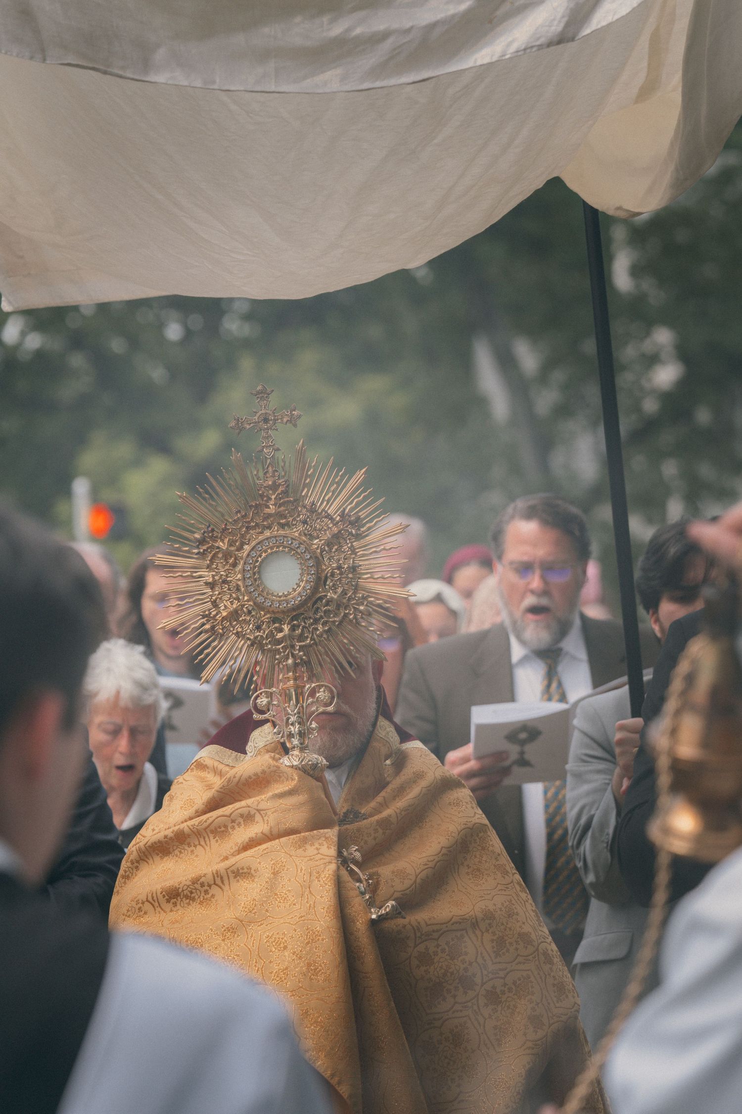 Priest in a gold veil carrying the monstrance through a crowd during a Corpus Christi procession