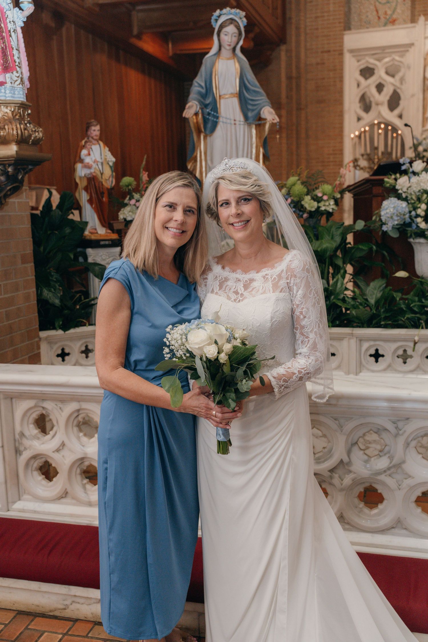 Bride with her bridesmaid in blue beneath a statue of Mary at the altar