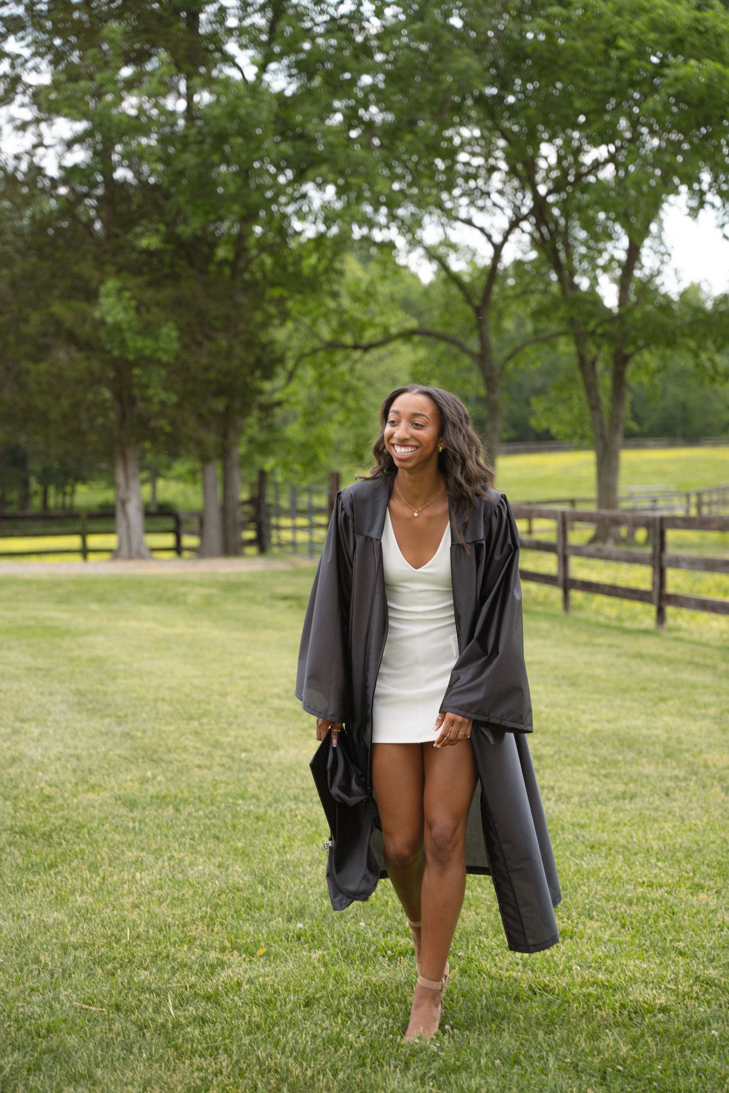 Graduate in an open black gown walking through a green pasture