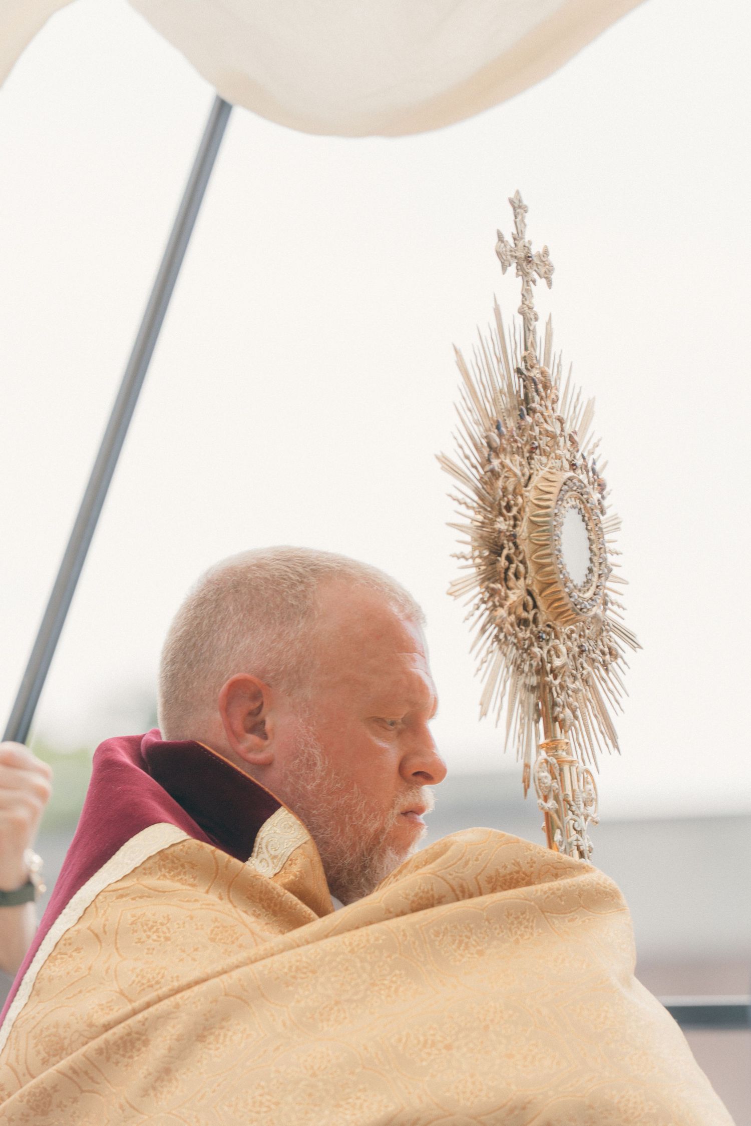 Priest in a gold vestment carrying the Blessed Sacrament in a monstrance during Eucharistic procession