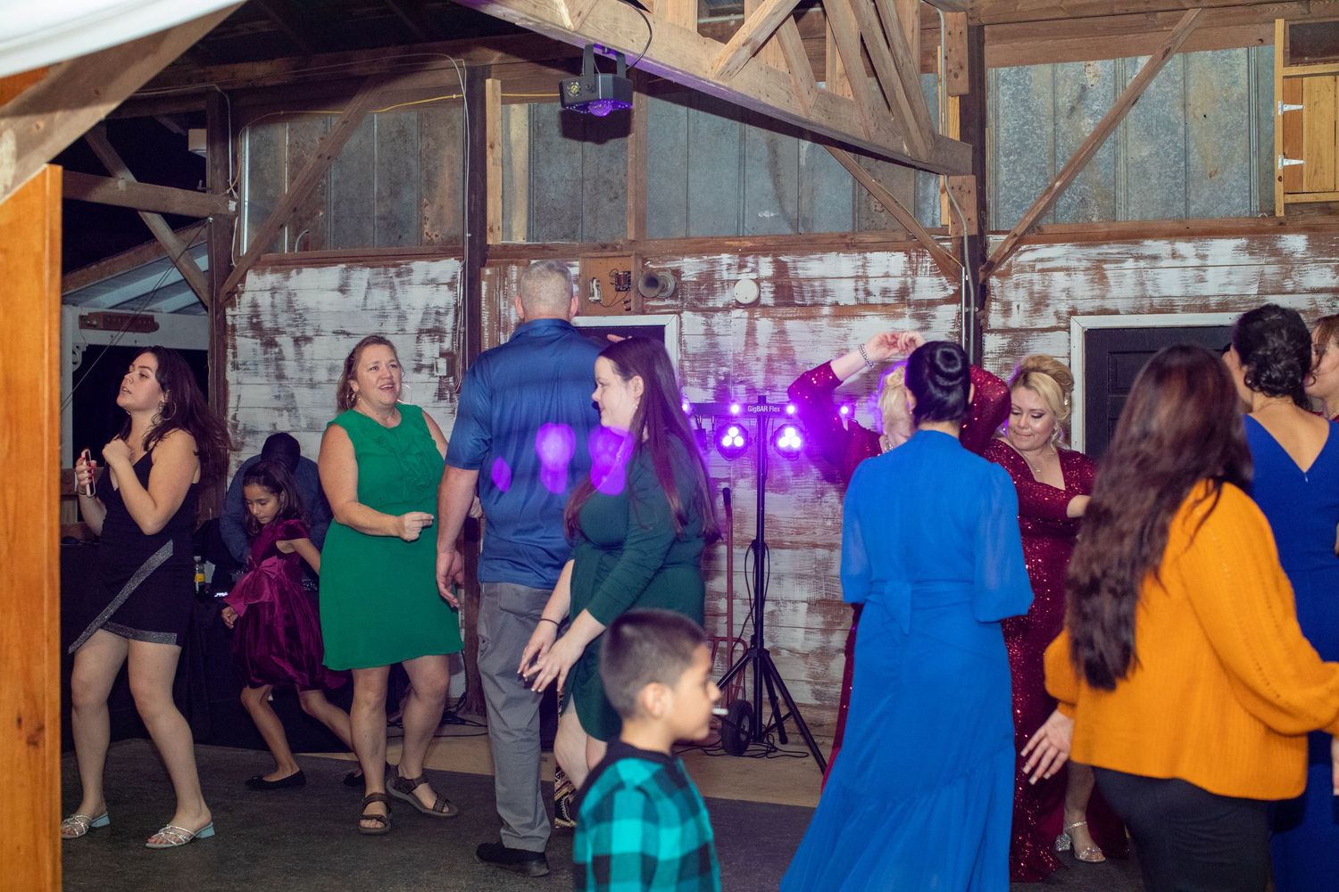 Guests dancing under colorful lights at a rustic barn wedding reception