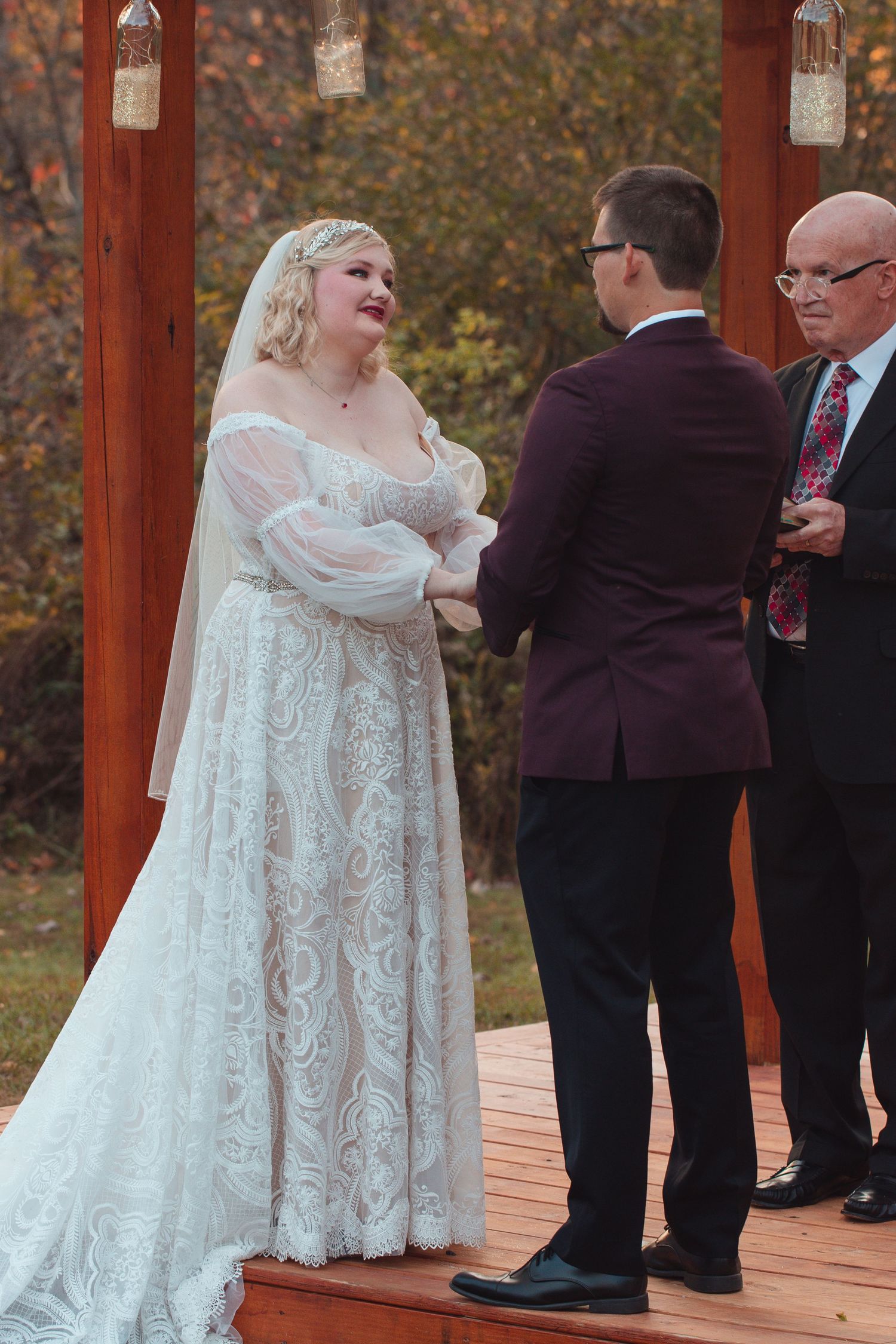 Bride and groom facing each other under the pergola as the officiant looks on