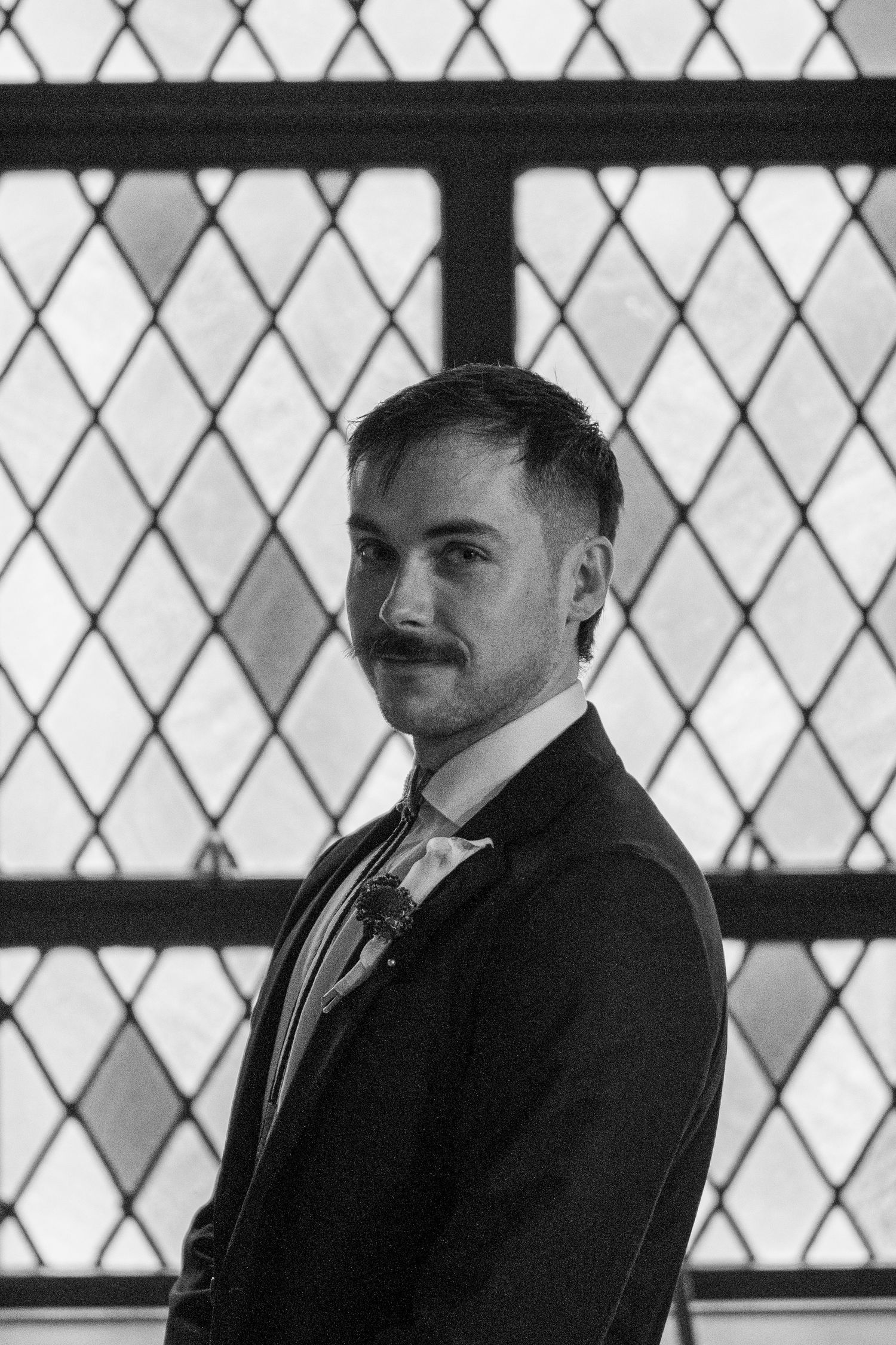 Groom standing before a leaded glass window before his Catholic wedding