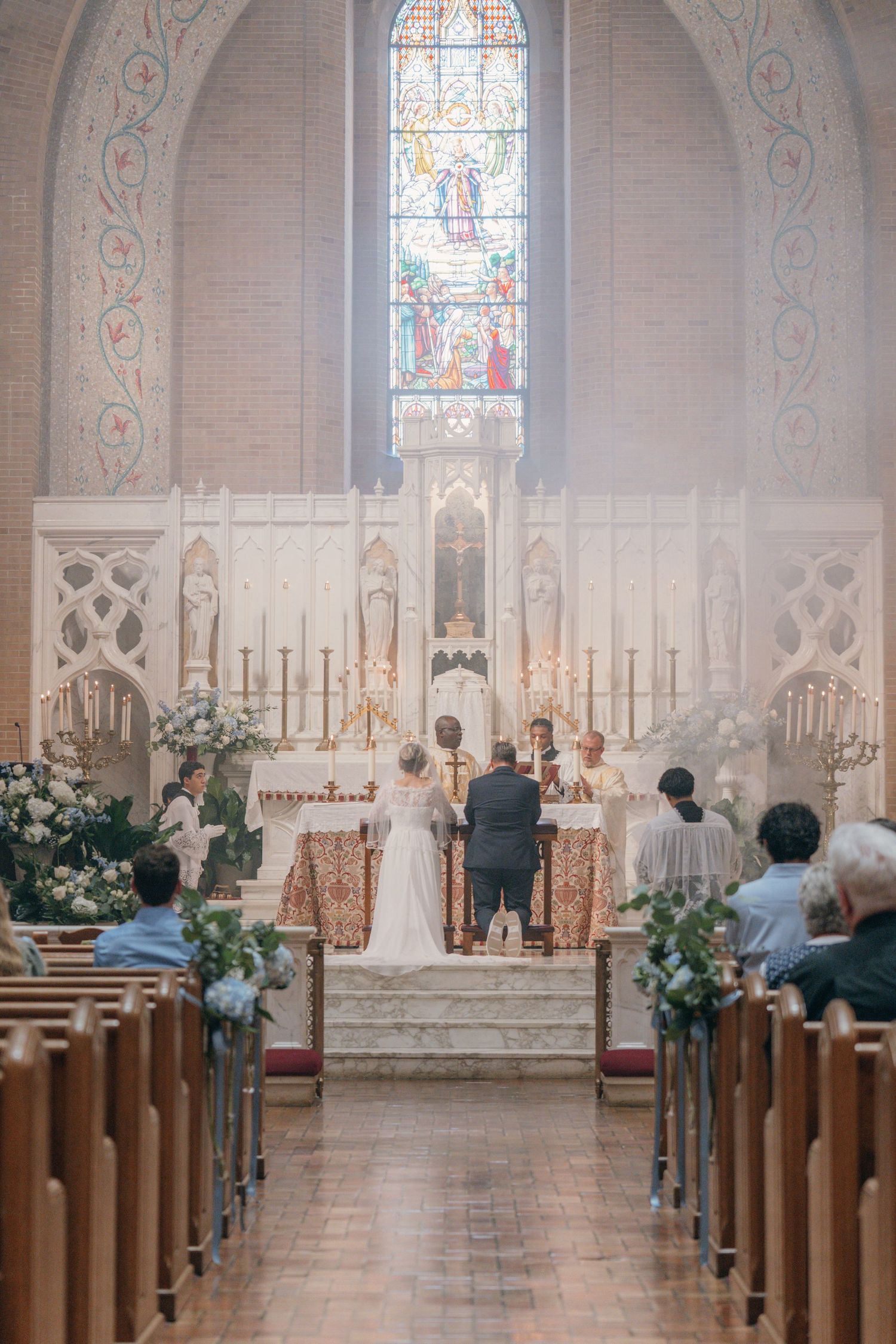 Catholic wedding ceremony seen from the center aisle with stained glass above the altar