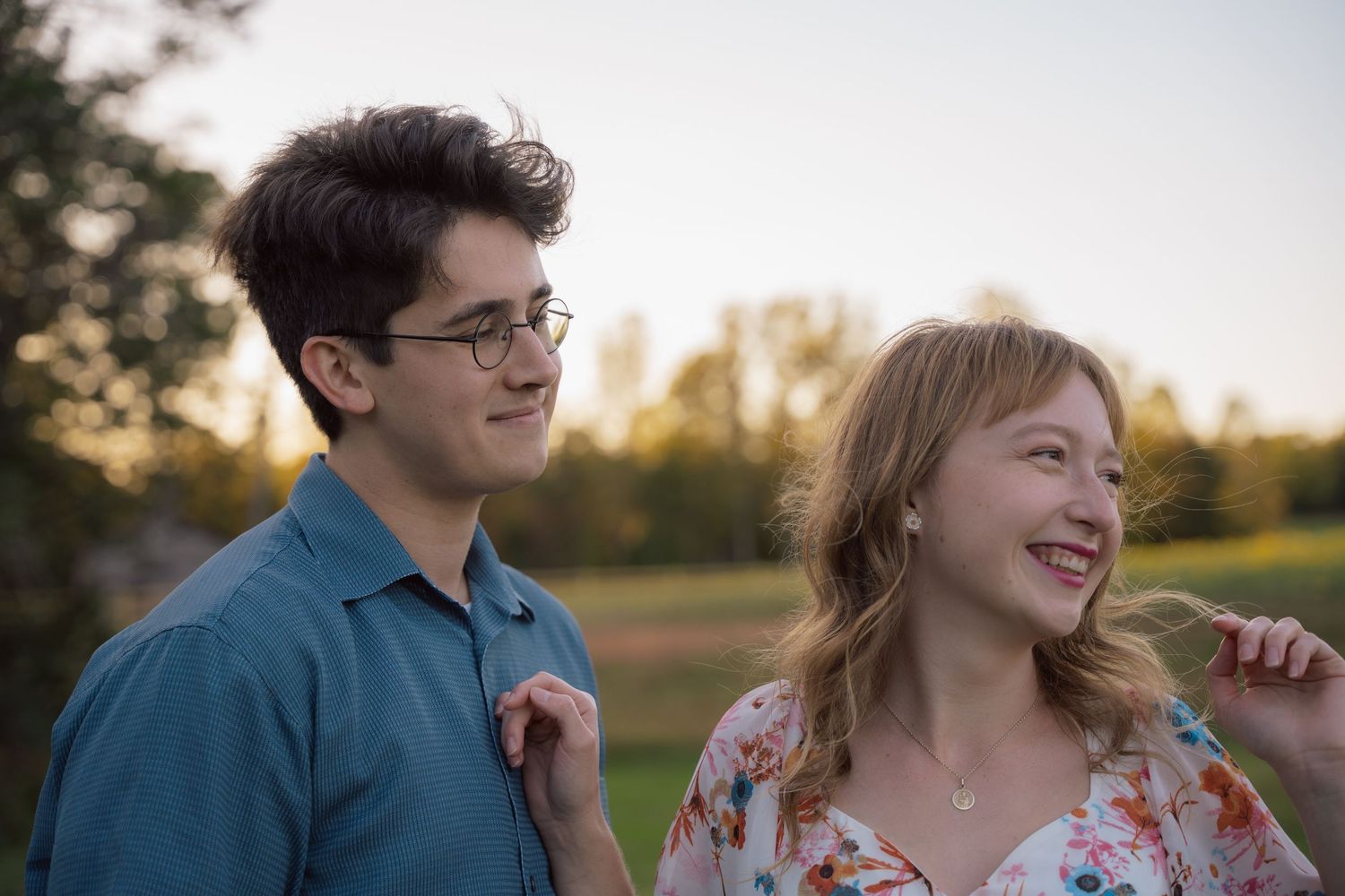 Couple sharing a laugh in a field during a golden hour engagement session