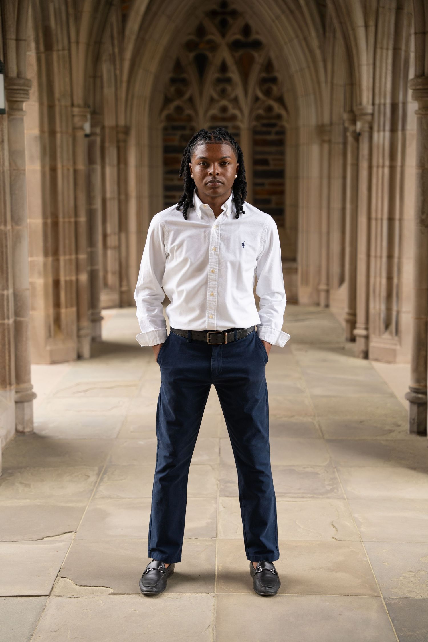 Graduate standing in the center of a vaulted stone cloister walkway