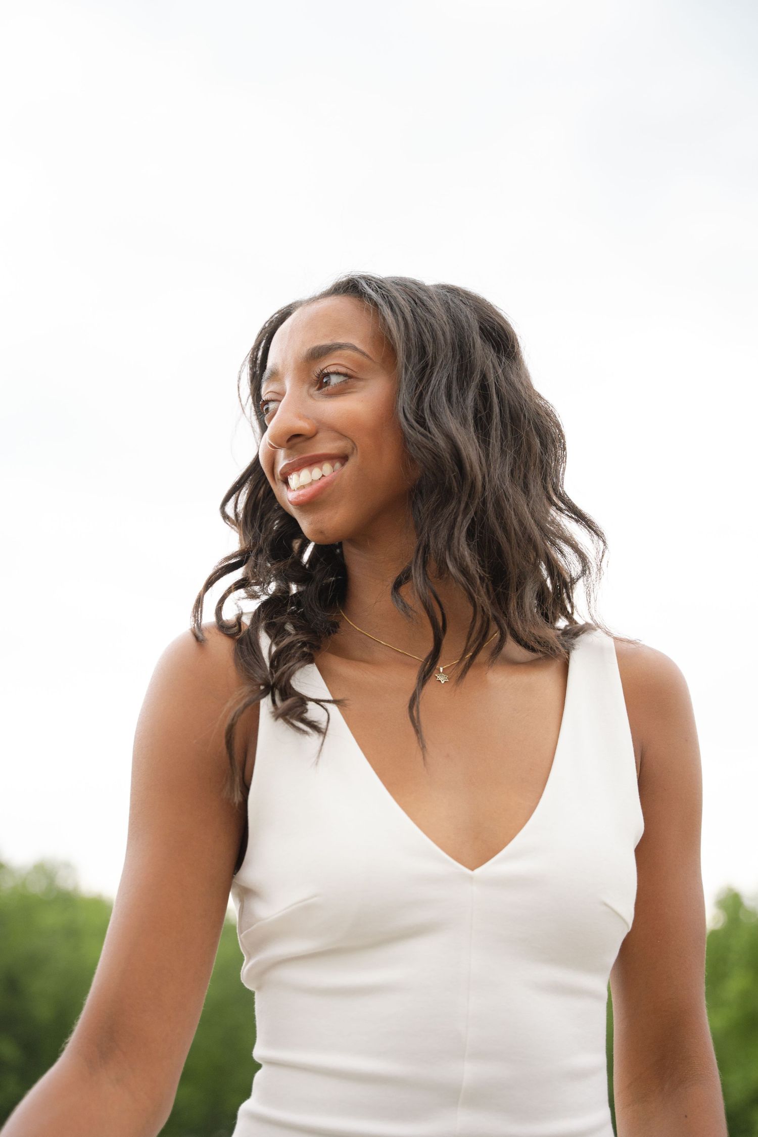 Portrait of a smiling graduate in a white dress with the countryside behind her