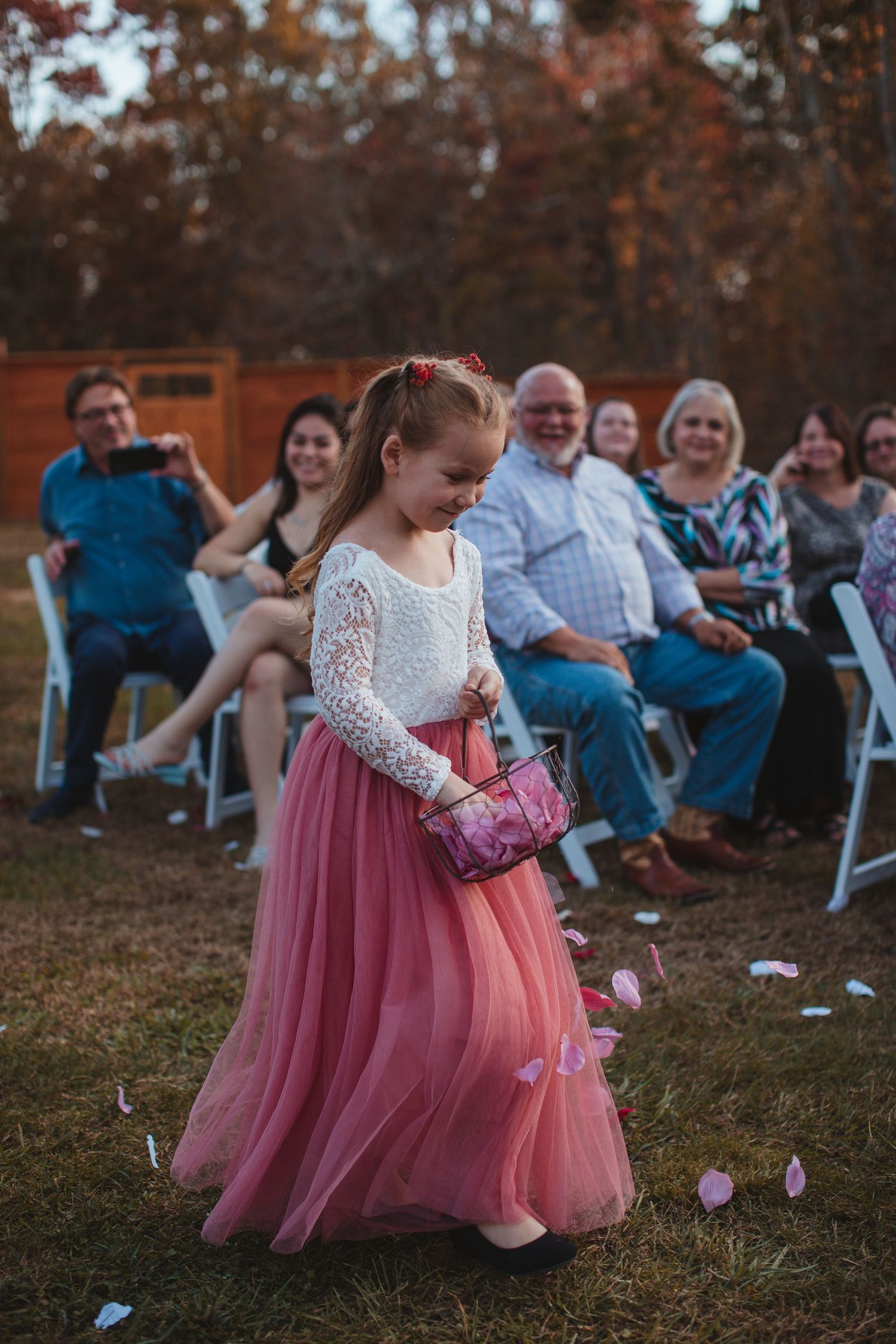Flower girl in a pink dress walking down the aisle at an outdoor wedding