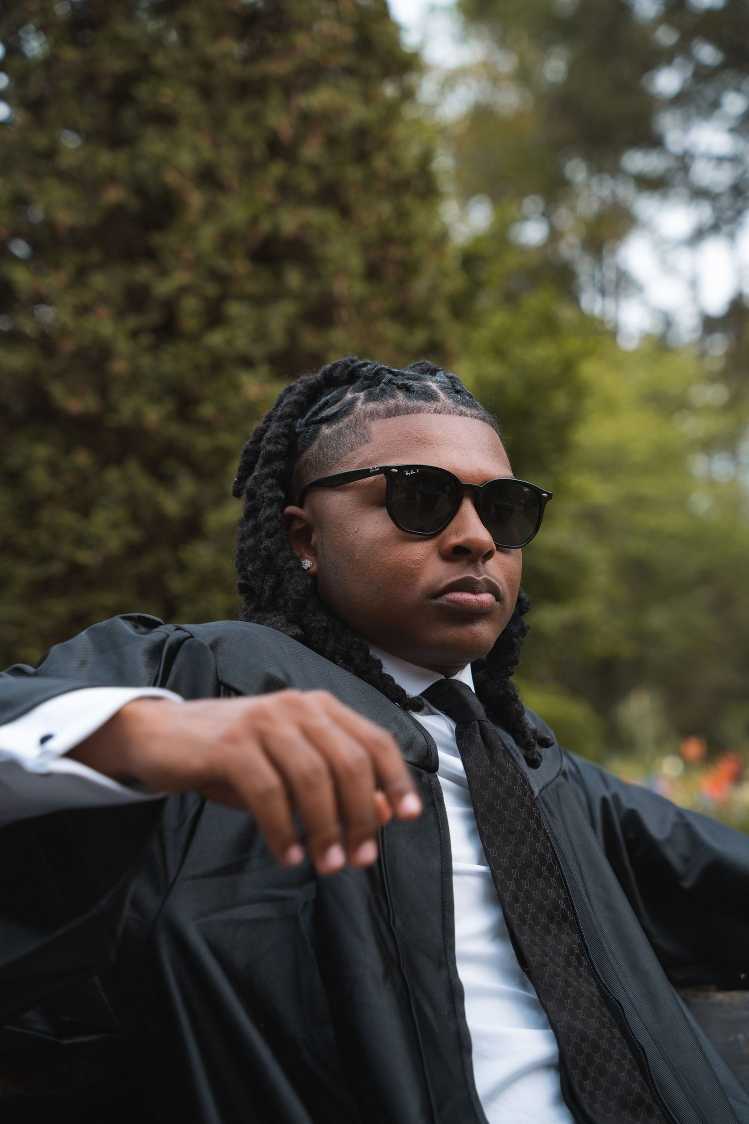 Graduate in a black gown and sunglasses relaxing in a garden