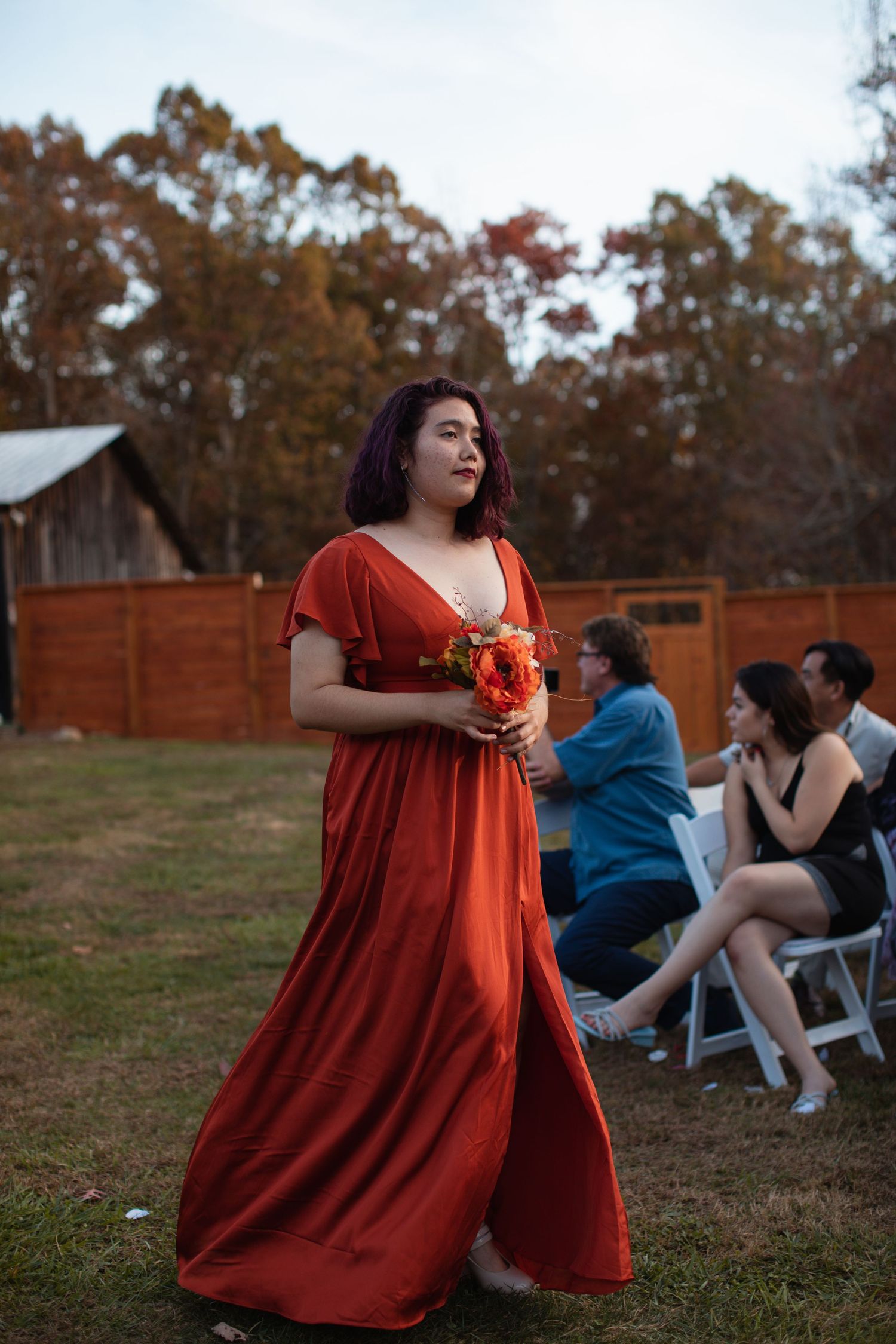 Bridesmaid in a red gown walking down the aisle carrying flowers