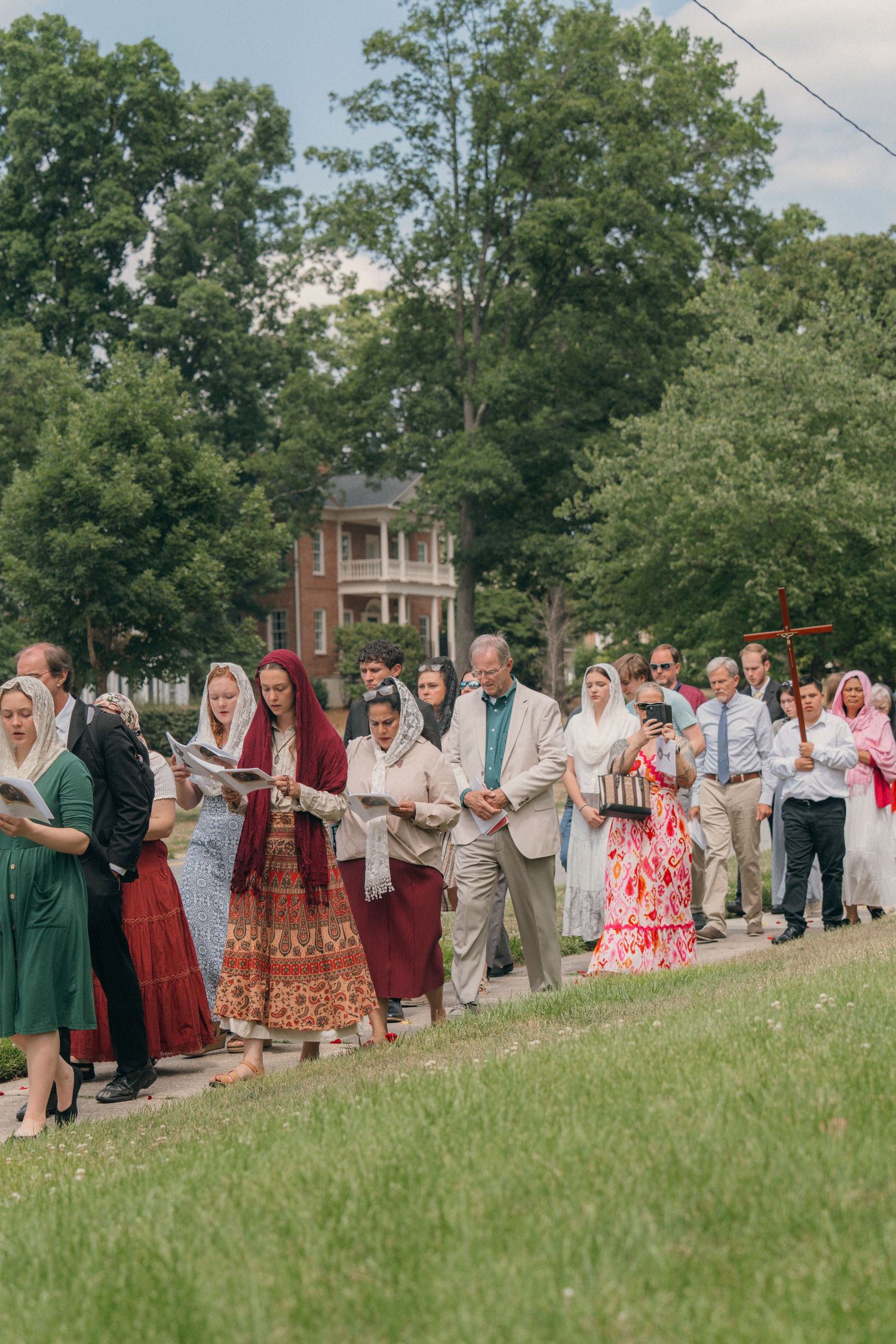 Parishioners in colorful dresses walking across a church lawn in a Corpus Christi procession