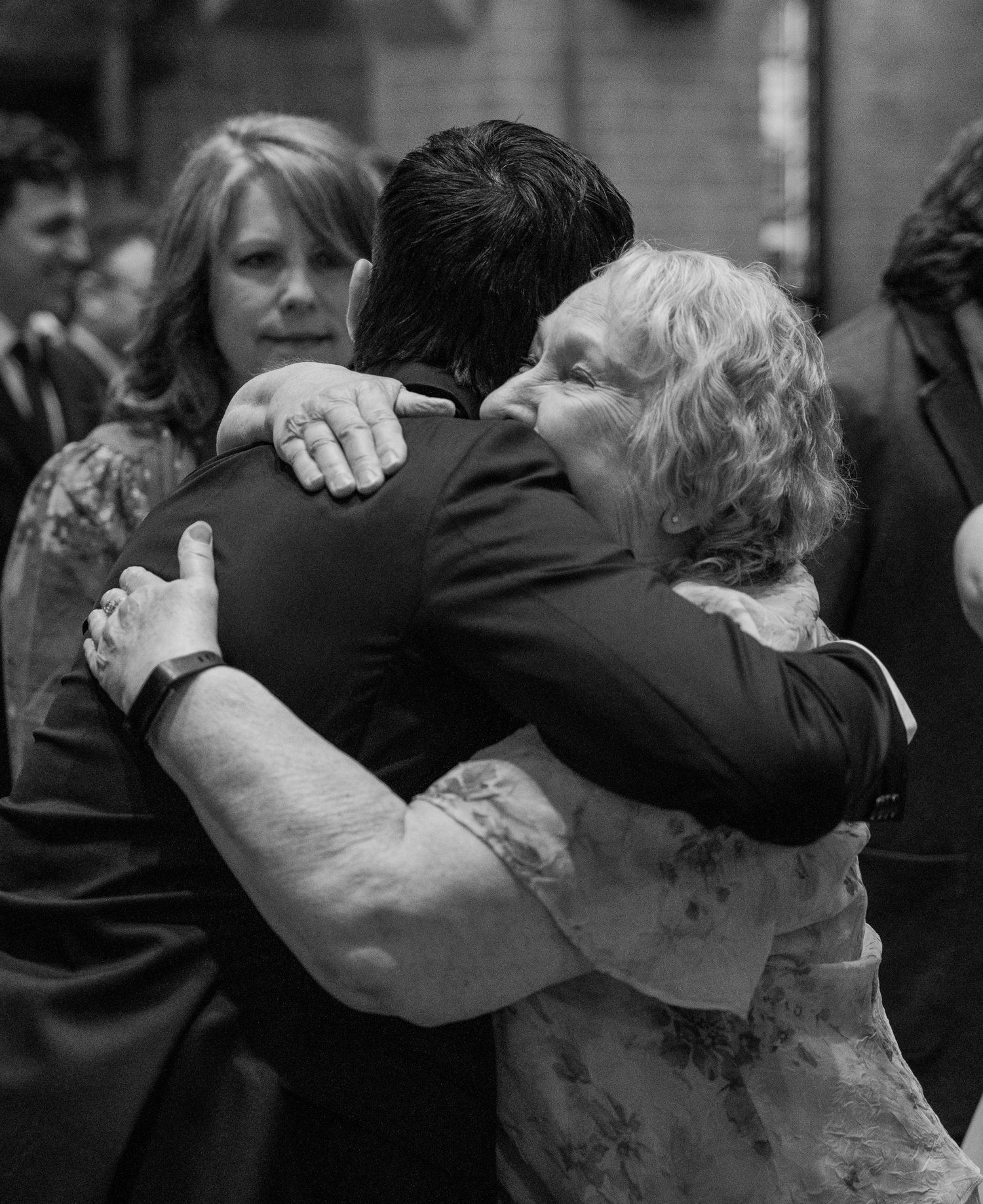 Black and white photo of the groom hugging a family member