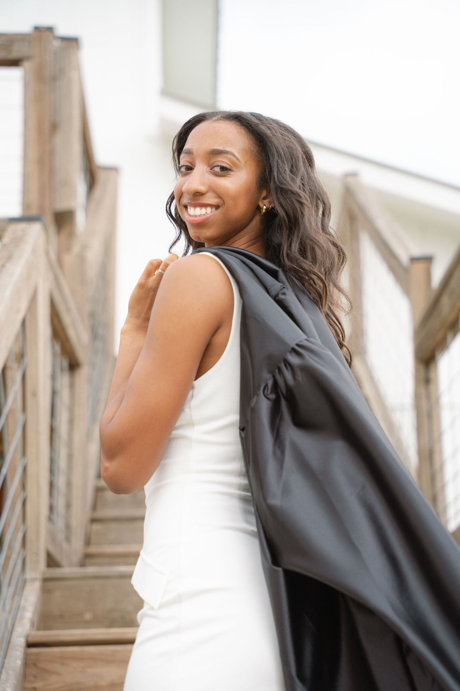 Graduate holding her cap and gown over her shoulder on a rustic wooden deck