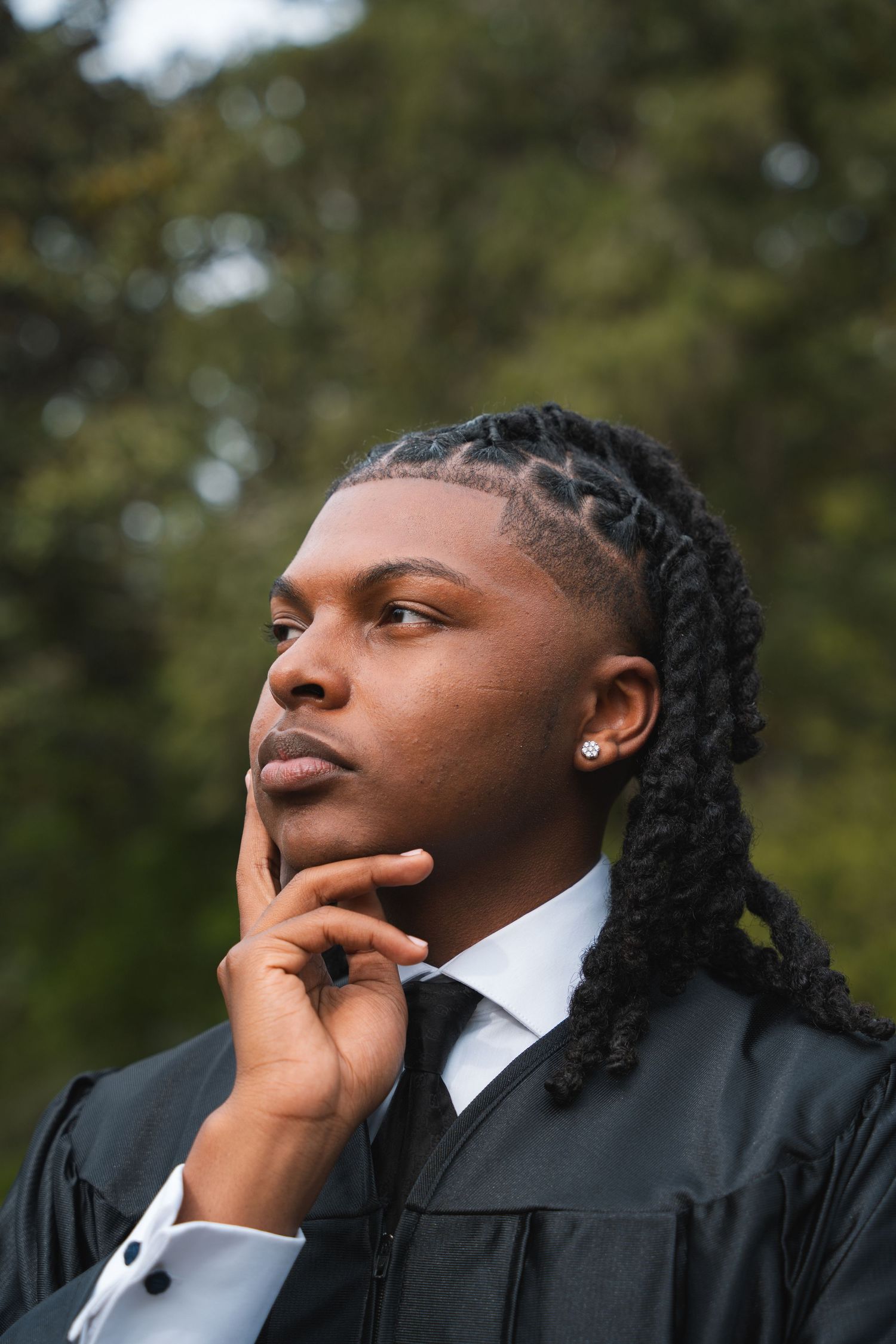 Graduate in a black gown with hand on chin, looking away thoughtfully