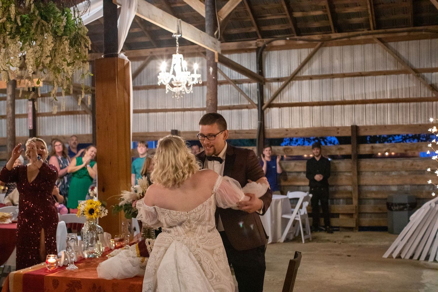 Bride and groom dancing under chandeliers in a rustic barn reception