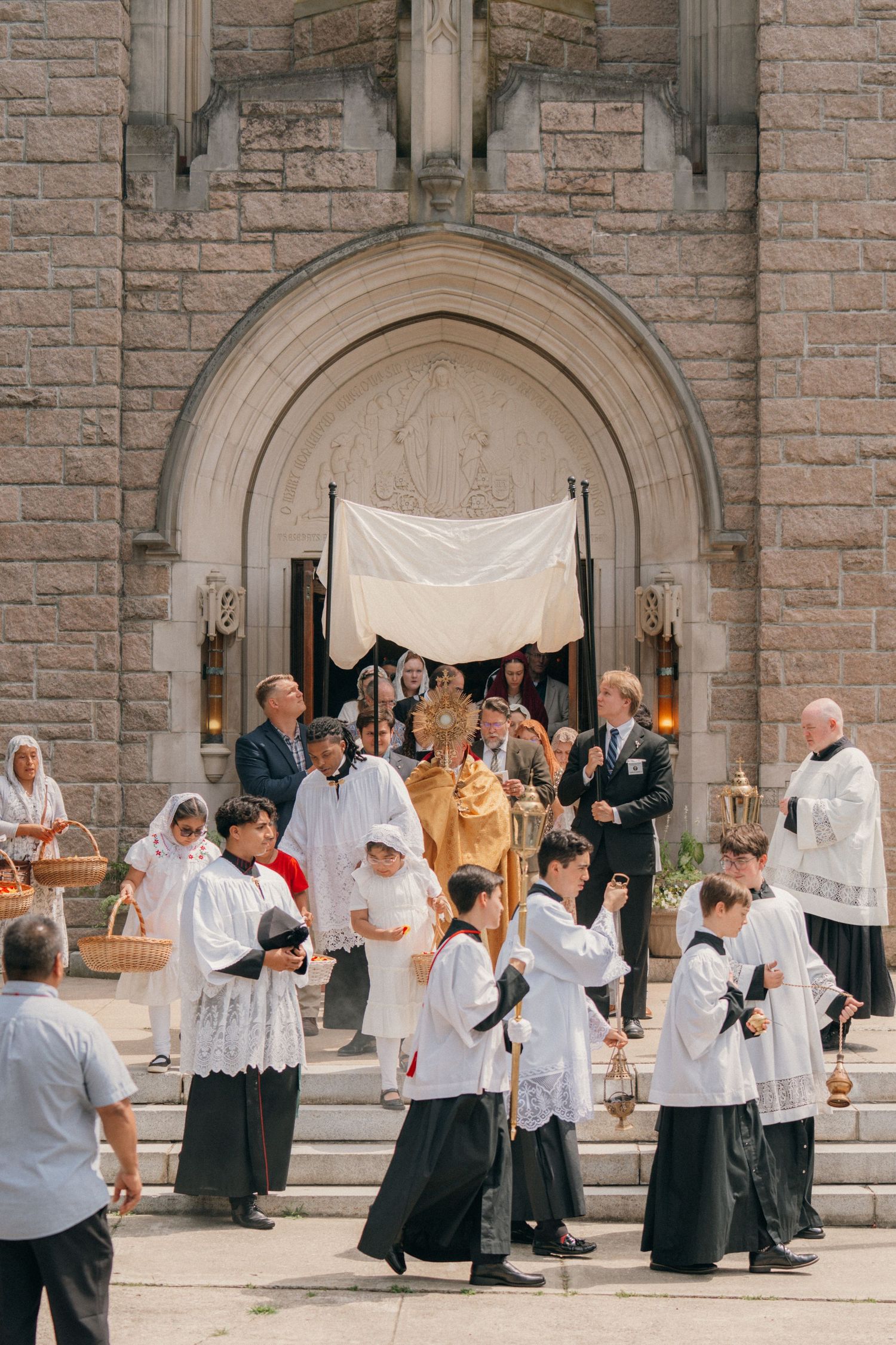 Altar servers and faithful kneeling on the church steps for Benediction during Corpus Christi