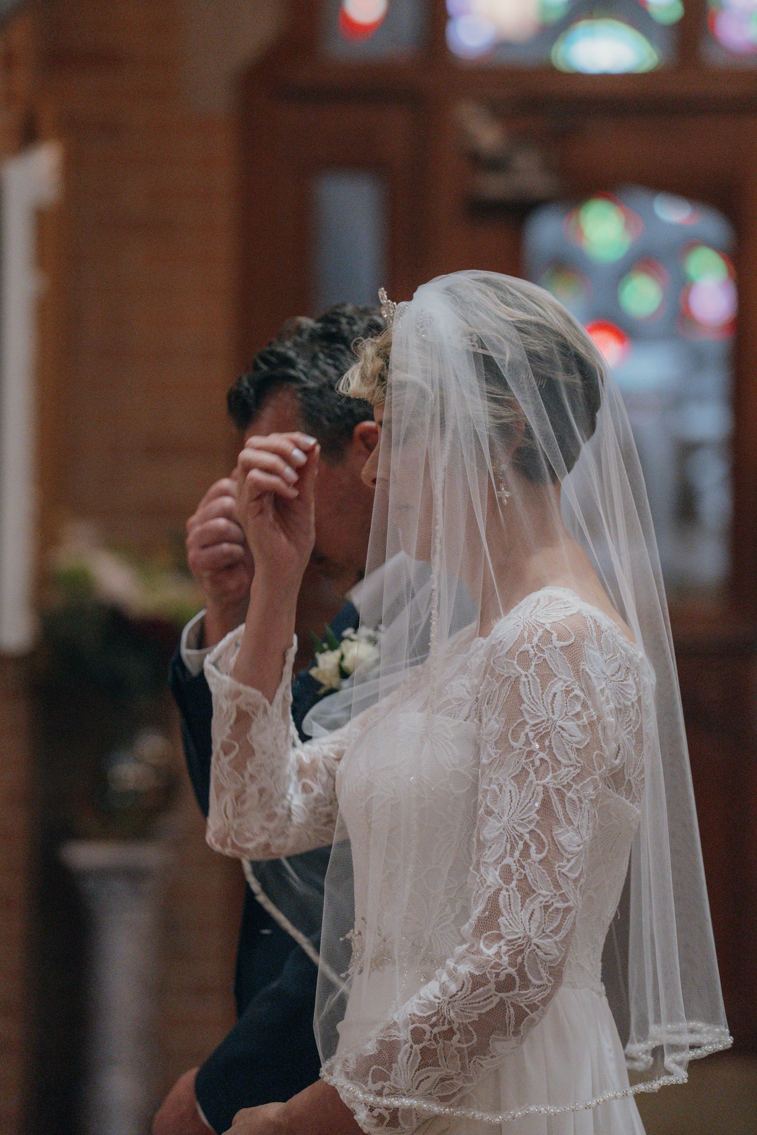 Bride in a lace veil wiping away a tear beside her father